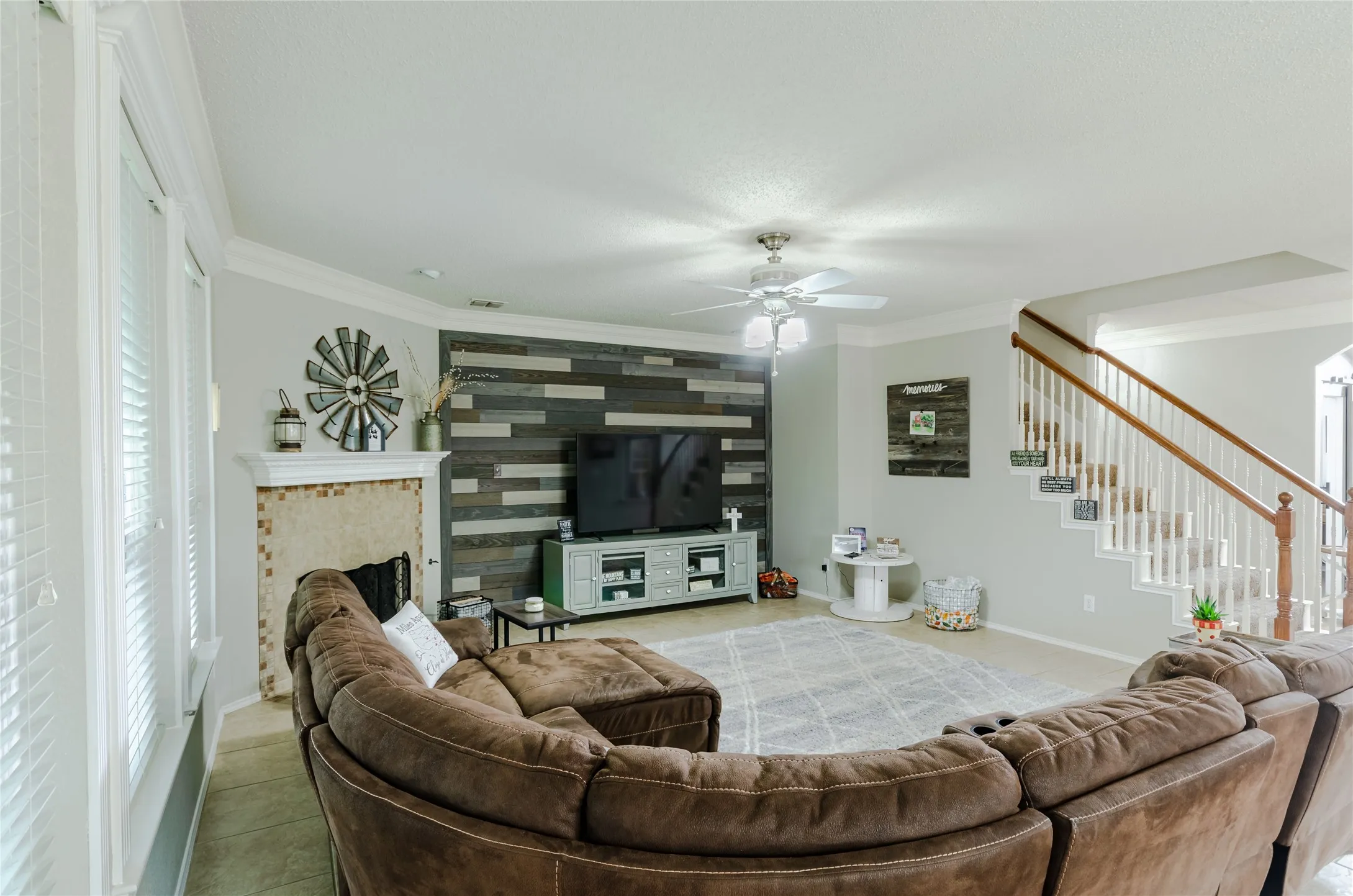 Living area featuring a accent wall, a ceiling fan with light, and a staircase with wood handrails and white balusters