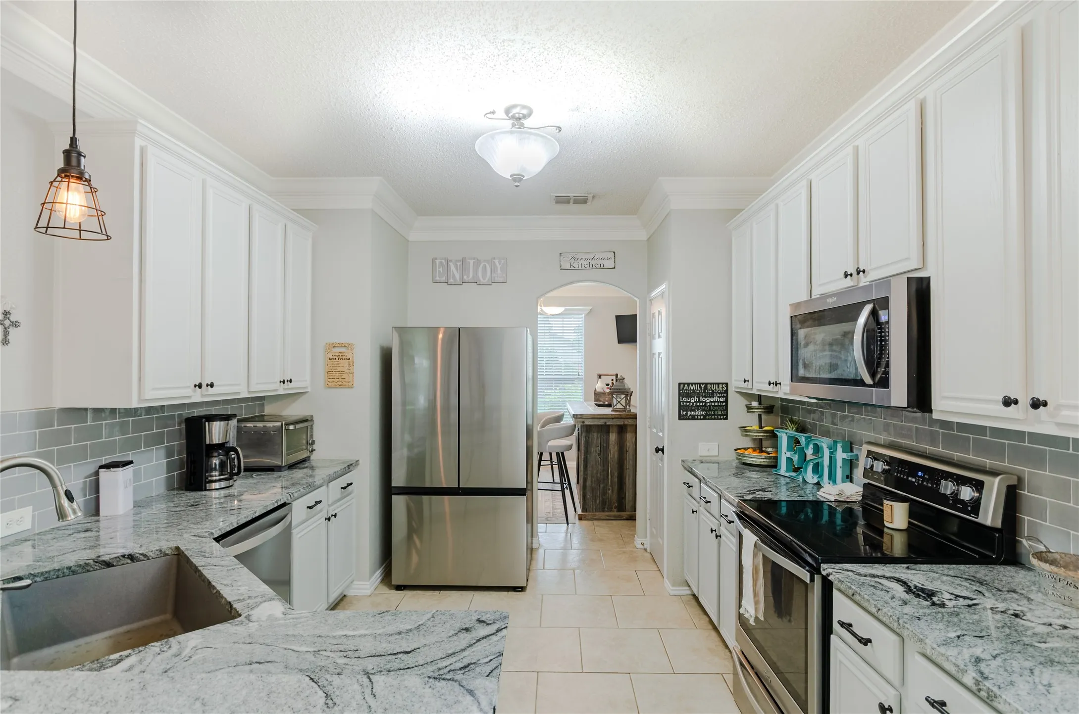 Kitchen featuring white cabinetry, light-colored granite countertops, a gray subway tile backsplash, and stainless steel appliances including a built-in microwave, refrigerator, and range