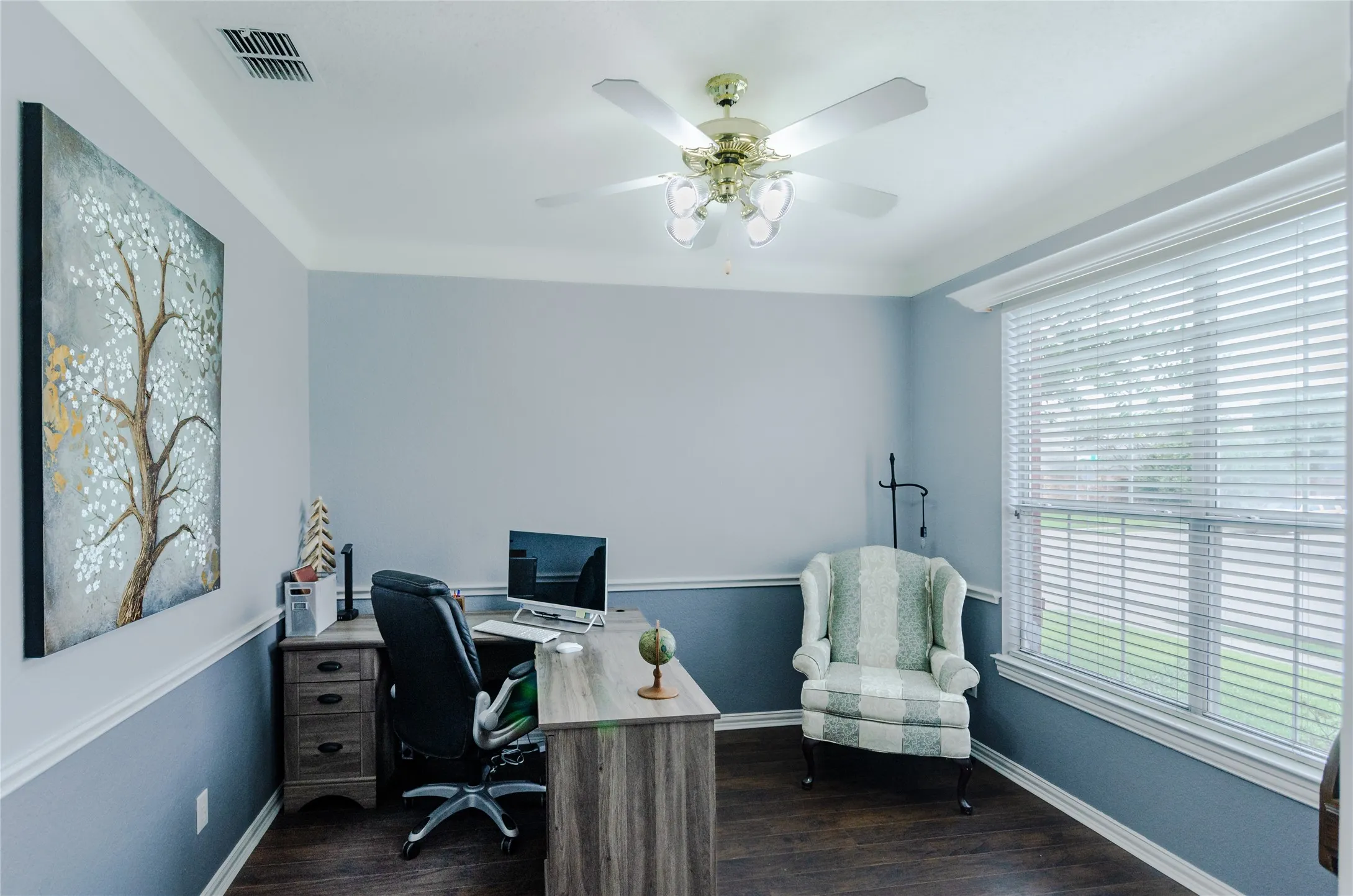 Dedicated office featuring wood-finish flooring, a large window with horizontal blinds, and a ceiling fan with integrated lighting