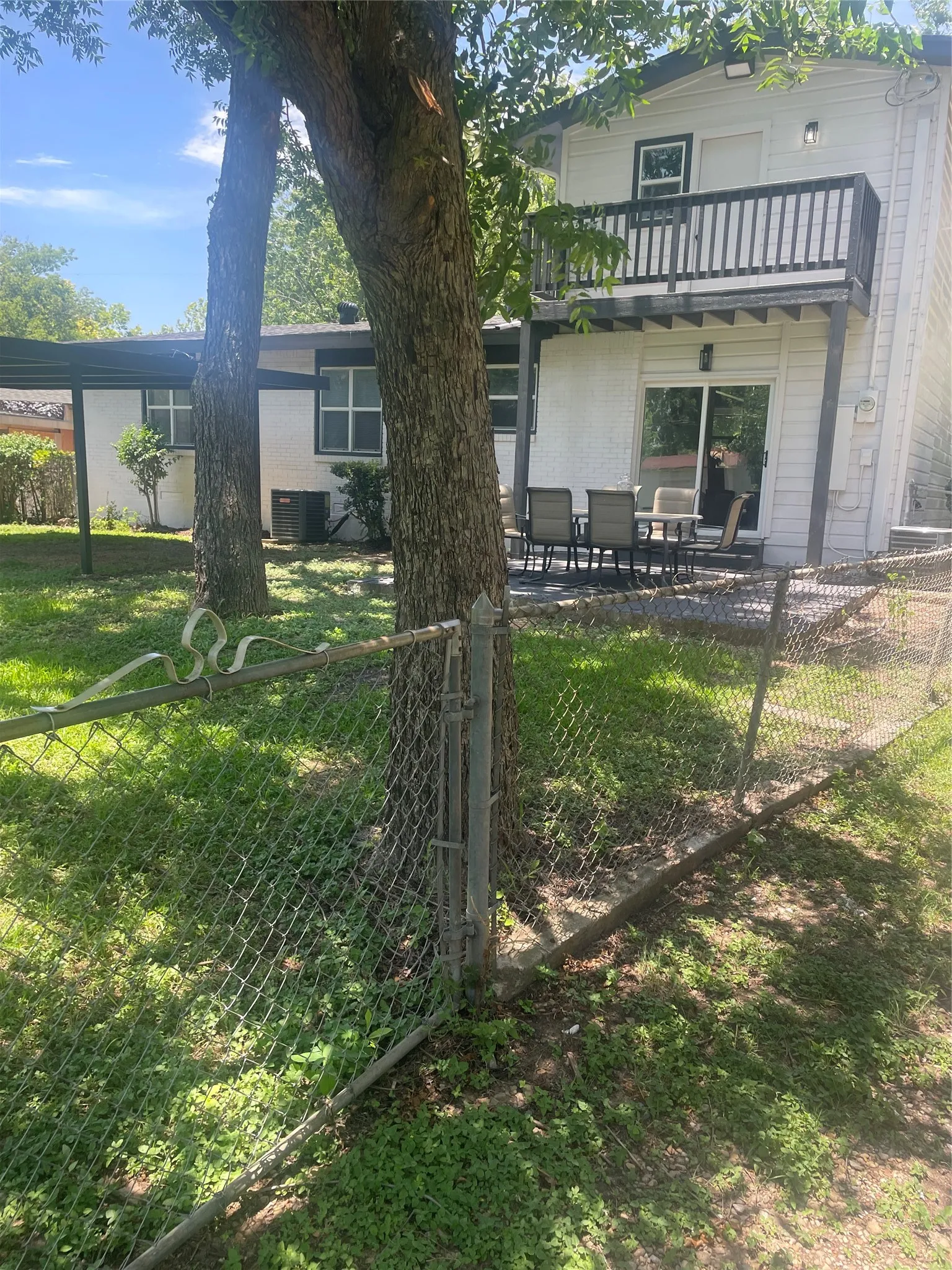 Rear exterior featuring a ground-level patio, a second-story balcony with dark railings, and a chain-link fence