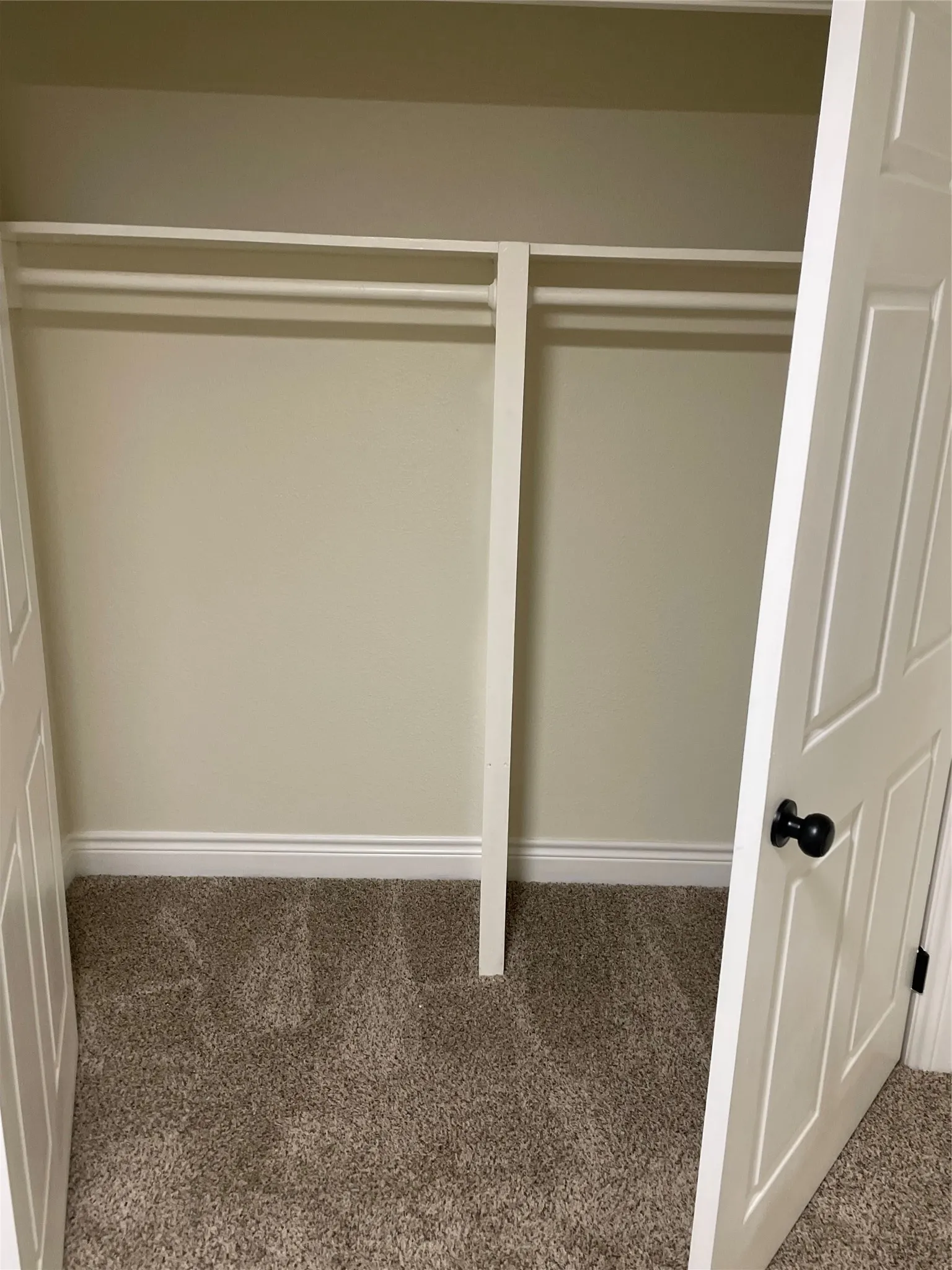 Recessed closet featuring dual hanging rods, light beige wall paint, white baseboards, and neutral-toned carpeting