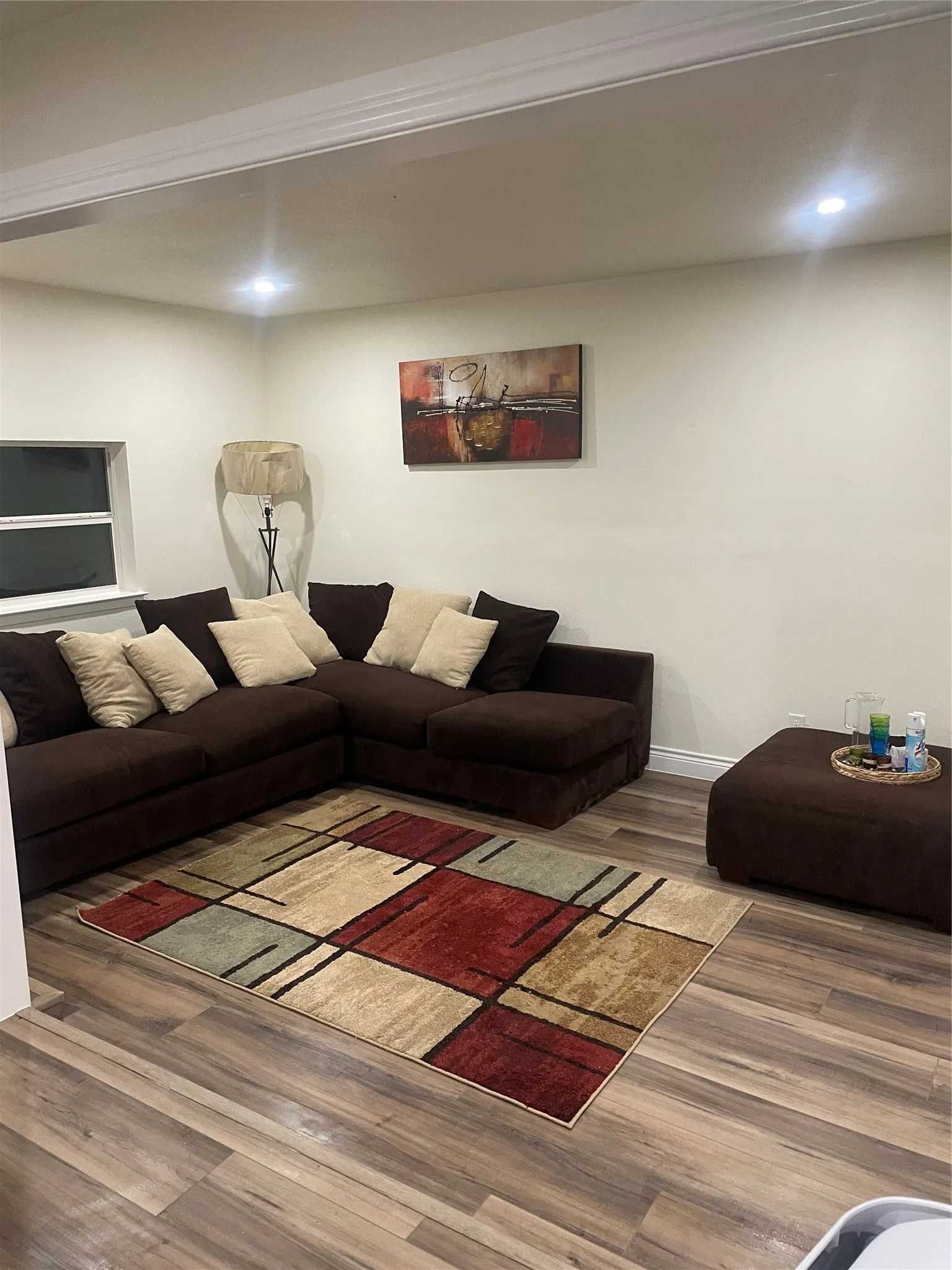 Spacious living area featuring wood-finish flooring, recessed lighting, and a window providing natural light