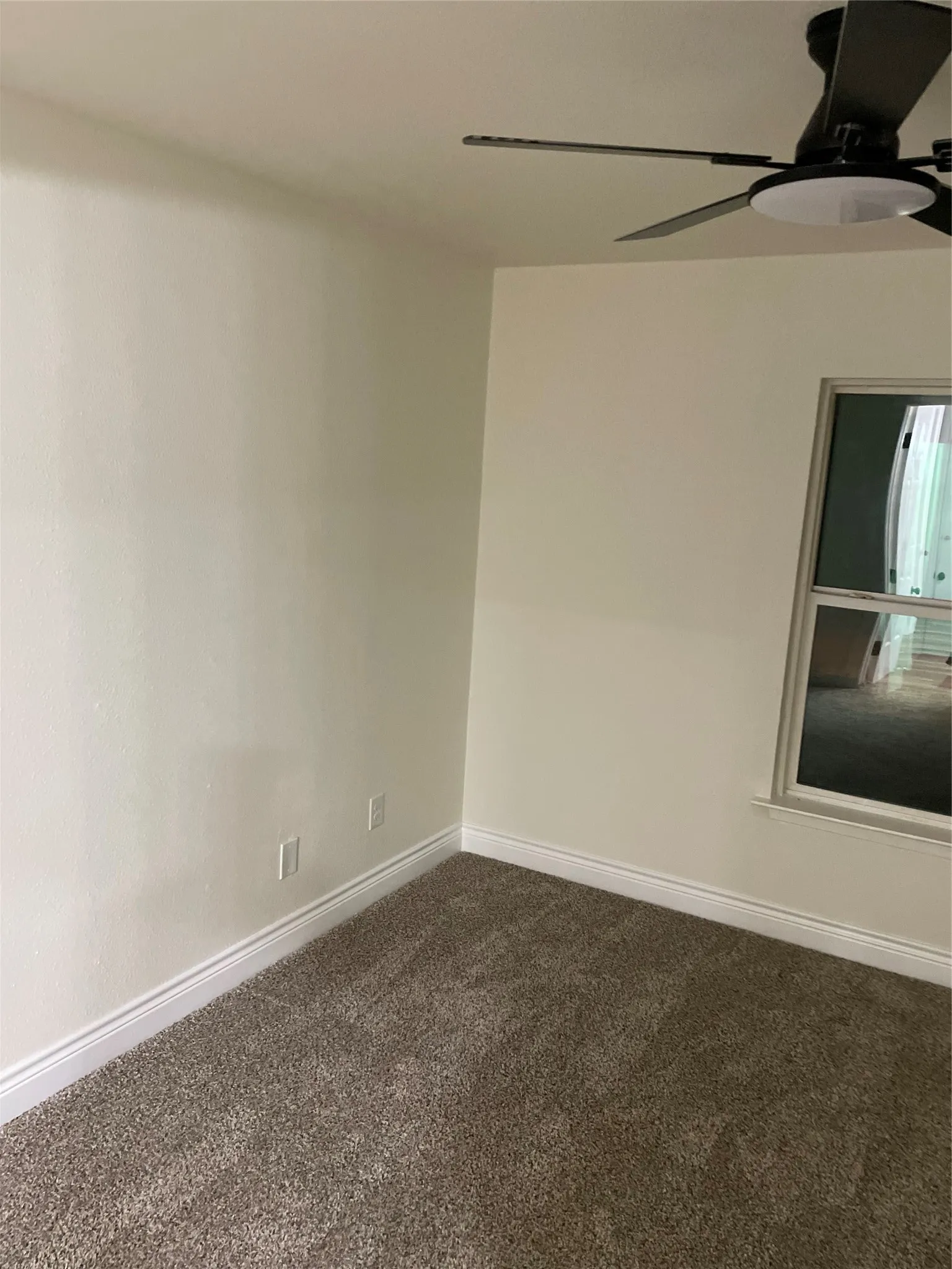 Carpeted room featuring a ceiling fan, a window, and light-colored walls with white baseboards
