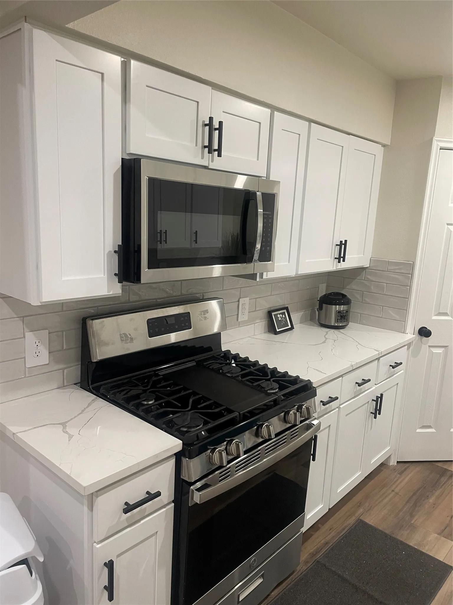 Contemporary kitchen featuring white shaker cabinetry with matte black hardware, stainless steel gas range, over-the-range microwave, solid surface countertops with subtle veining, and a light-toned subway tile backsplash
