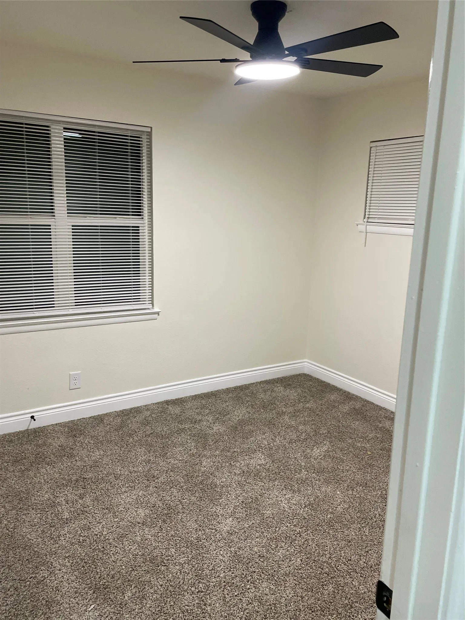 Bedroom featuring light-toned walls, textured carpeting, a modern ceiling fan with integrated lighting, and multiple windows with horizontal blinds