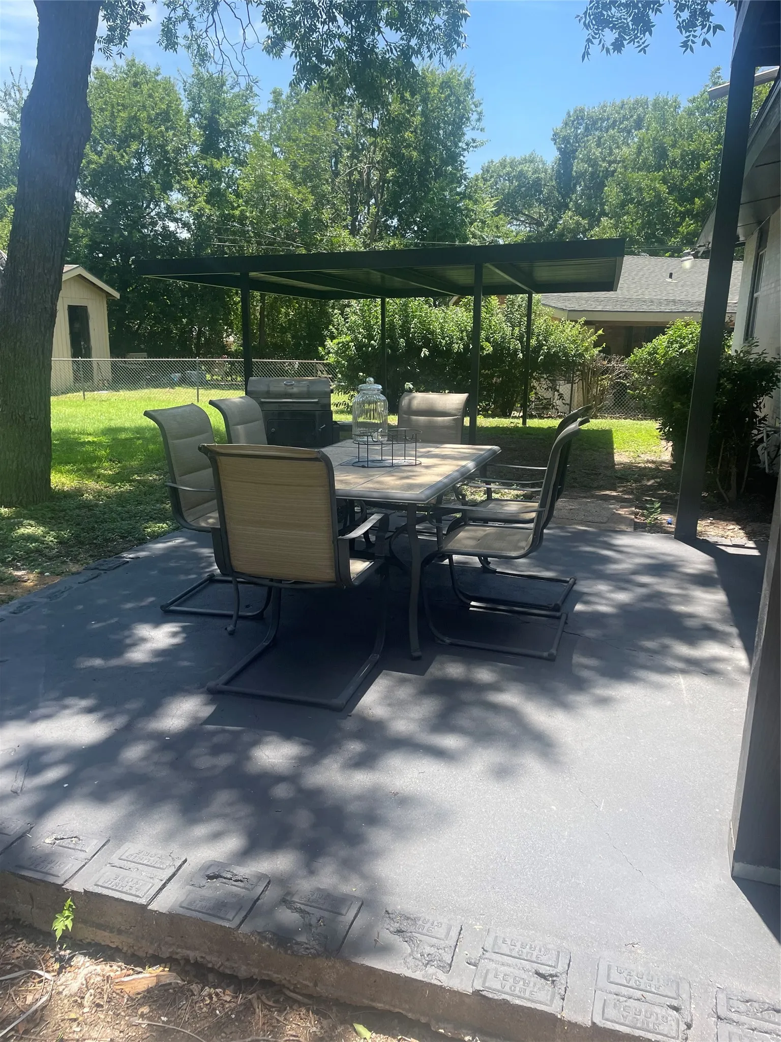 Outdoor patio featuring a metal pergola, a built-in grill, and mature trees