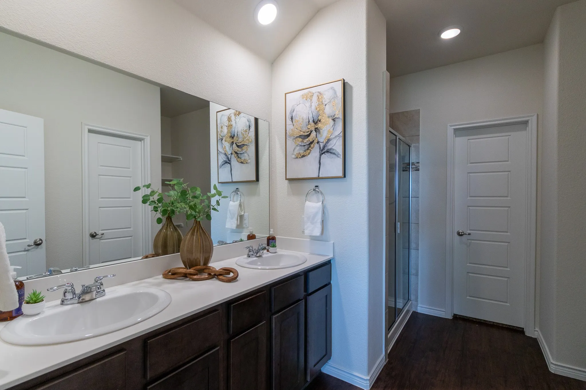 Double vanity with white oval sinks, chrome faucets, dark wood-finish cabinetry, and a large wall-mounted mirror