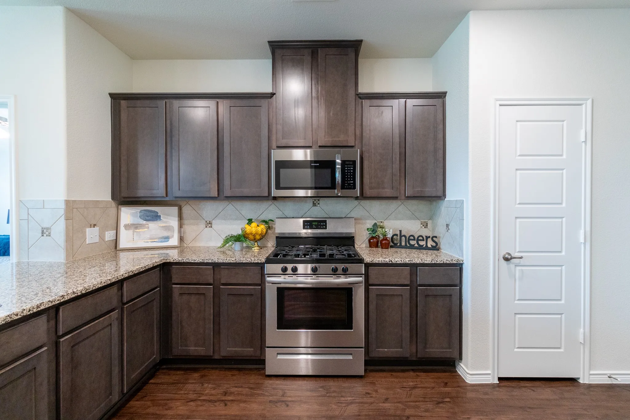 Modern kitchen featuring rich cabinetry, light speckled countertops, stainless steel appliances, a gas range, and wood-finish flooring