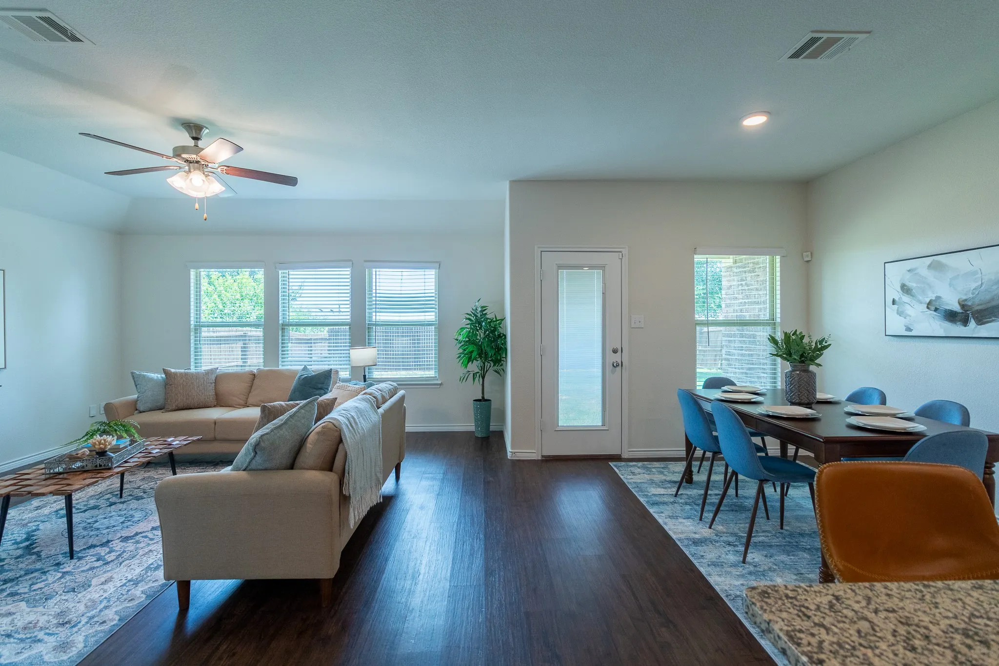 Open-concept living area featuring wood-finish flooring, a vaulted ceiling with a ceiling fan, and multiple windows with blinds