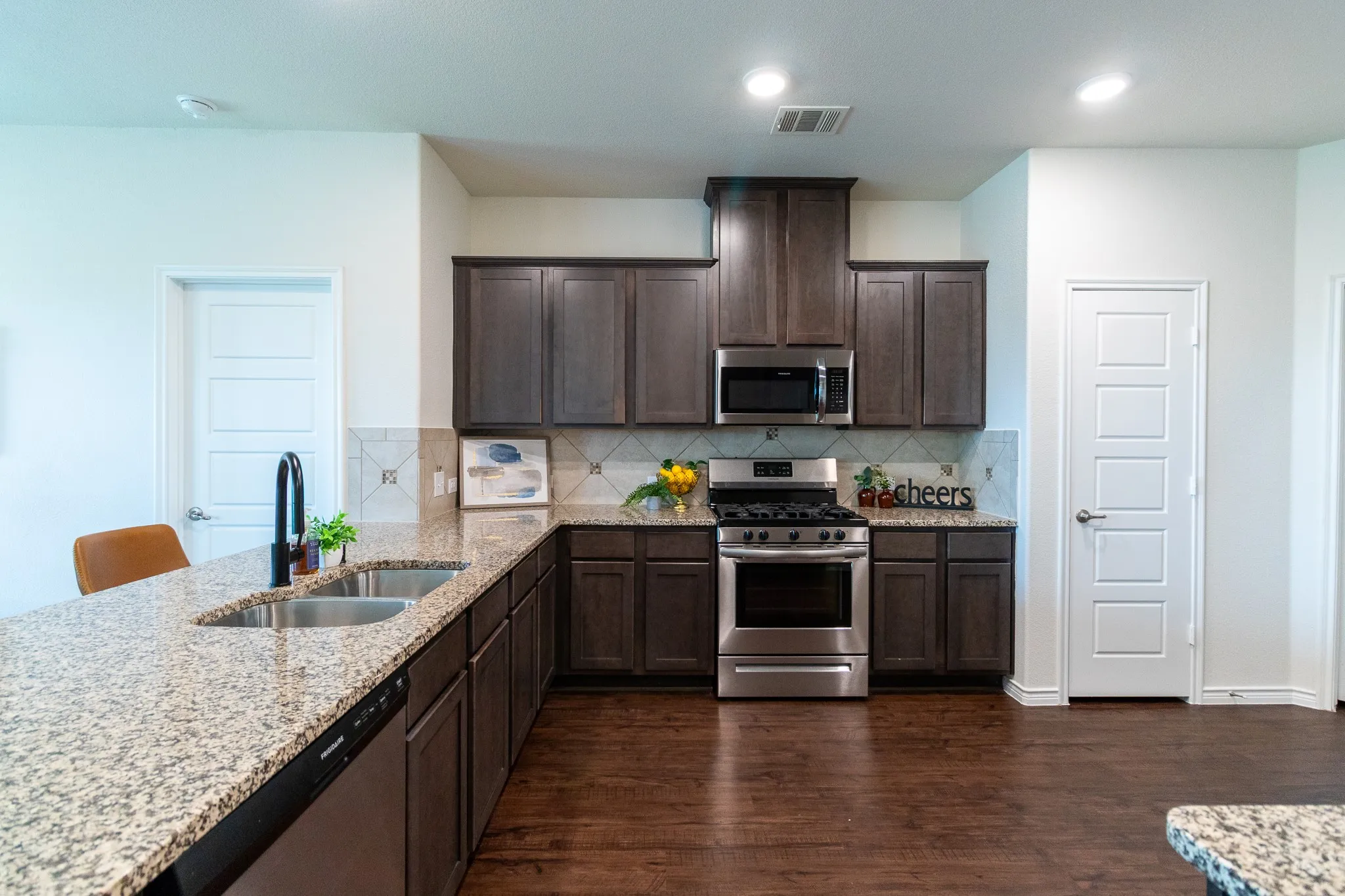 Kitchen featuring granite countertops, wood-finish flooring, stainless steel appliances, dark wood-finish cabinetry, and recessed lighting