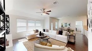 Spacious living area featuring wood-finish flooring, a ceiling fan, and multiple windows with blinds