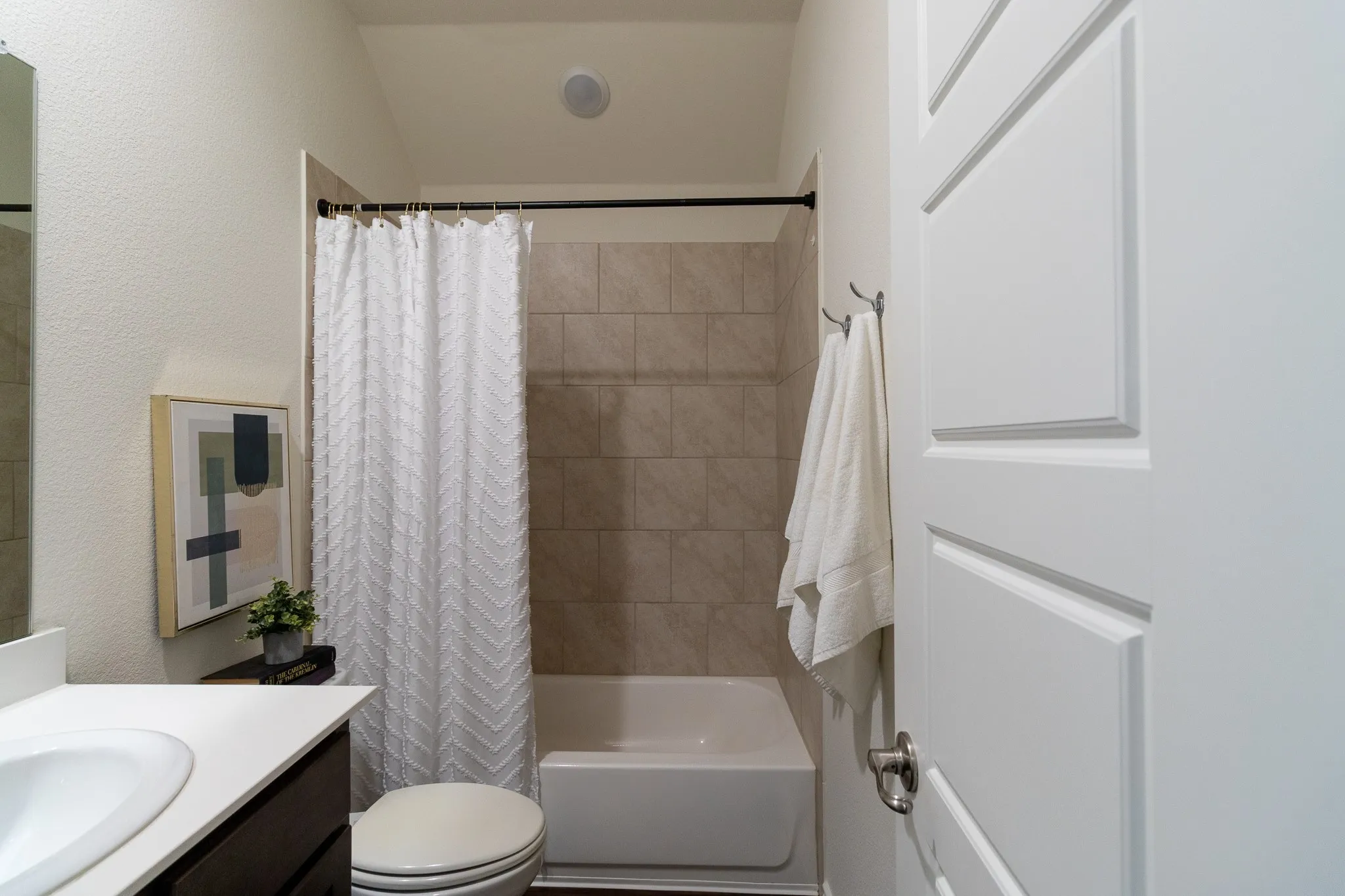 Bathroom featuring a white panel door, a single-sink vanity with white countertop, a toilet, and a combination tub and shower with tile surround