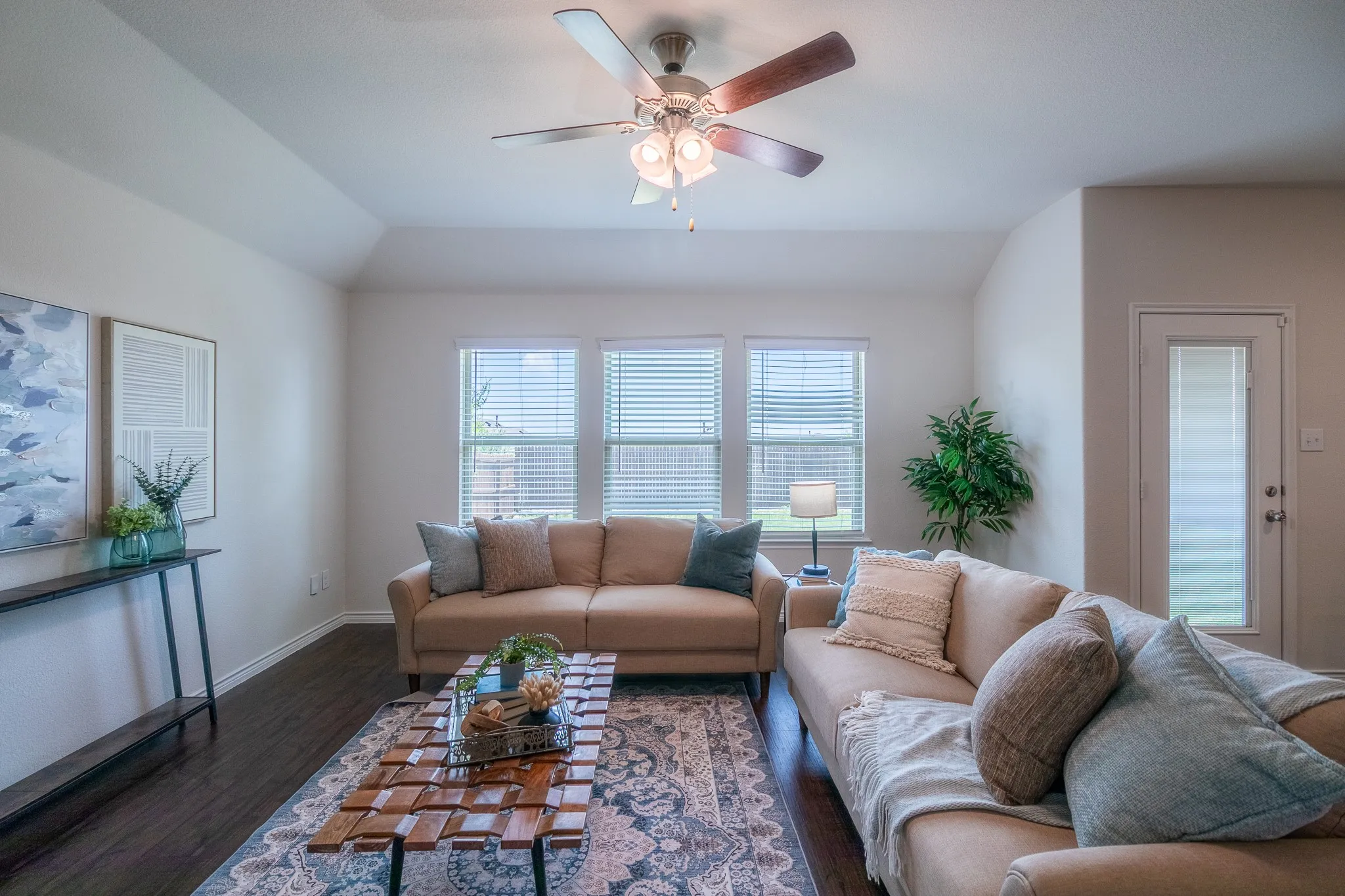 Living area featuring wood-finish flooring, a ceiling fan with integrated lighting, and multiple windows with blinds