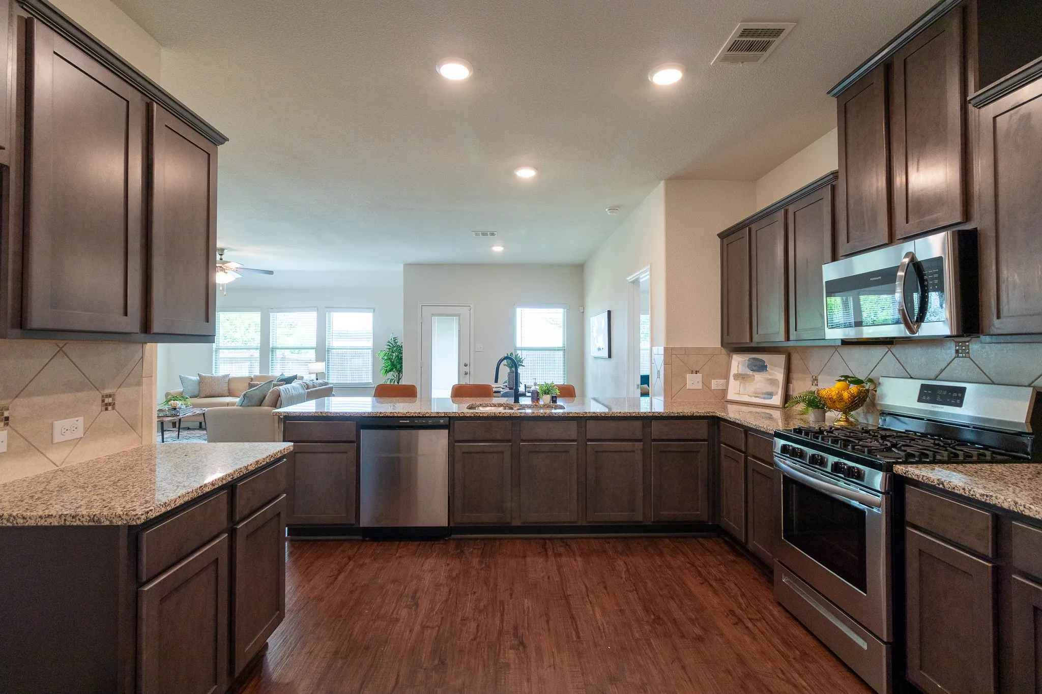 Open-concept kitchen featuring wood-finish flooring, dark wood cabinetry, light-toned countertops, and stainless steel appliances