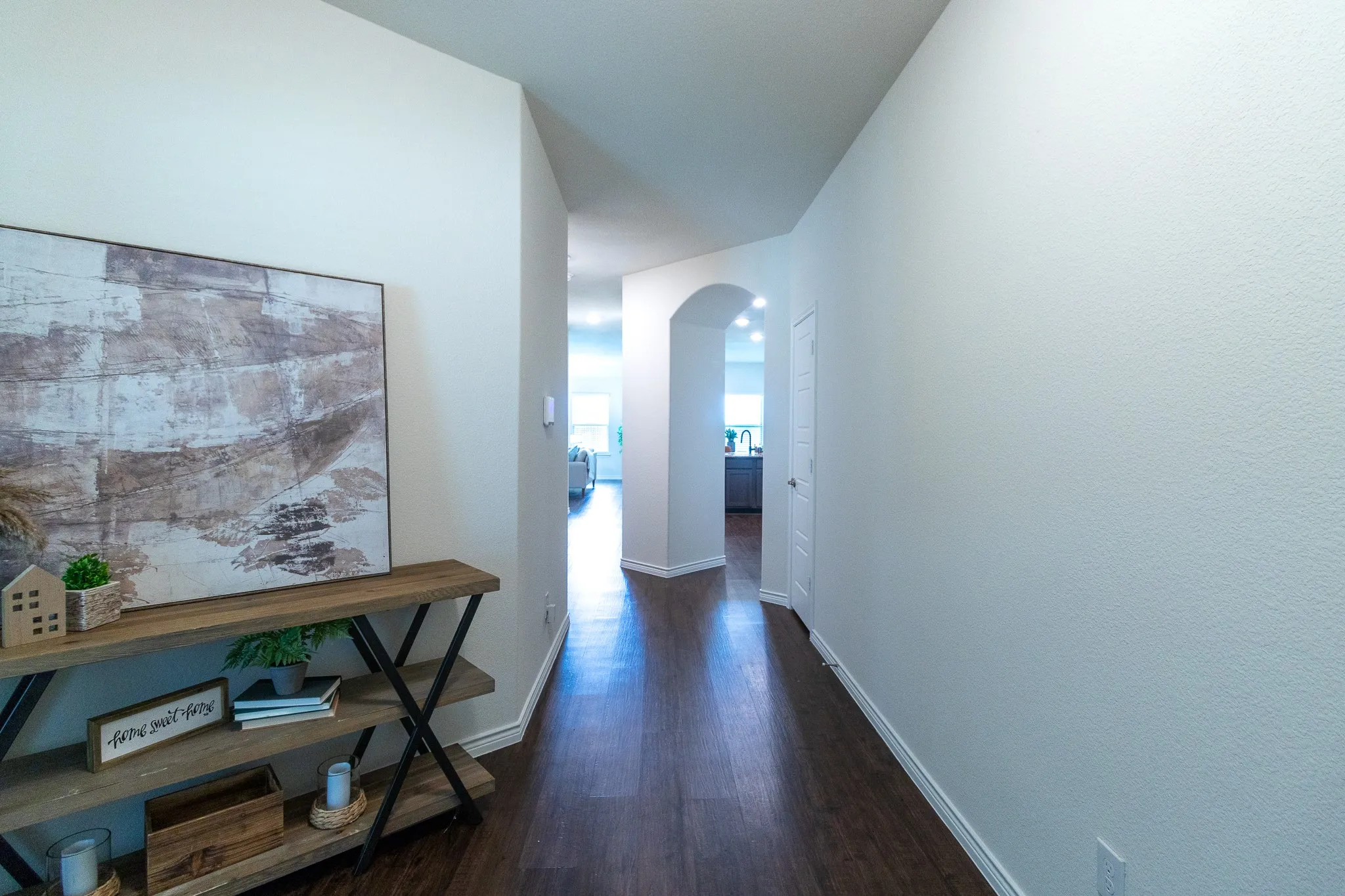 Hallway featuring wood-finish flooring, light-toned walls, and an arched doorway