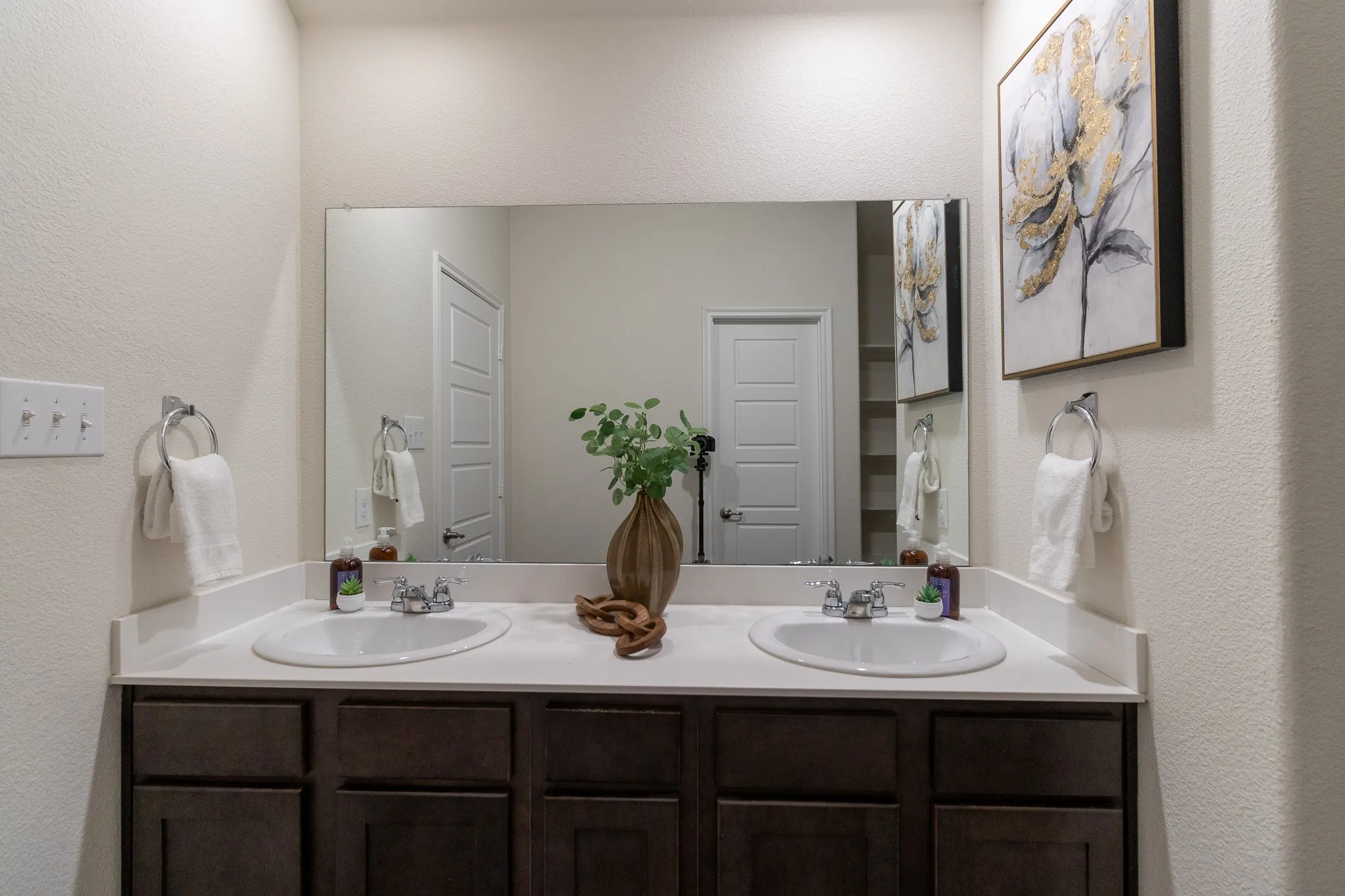 Dual undermount sinks set within a white countertop, featuring dark wood-finish cabinetry below and a large wall-mounted mirror