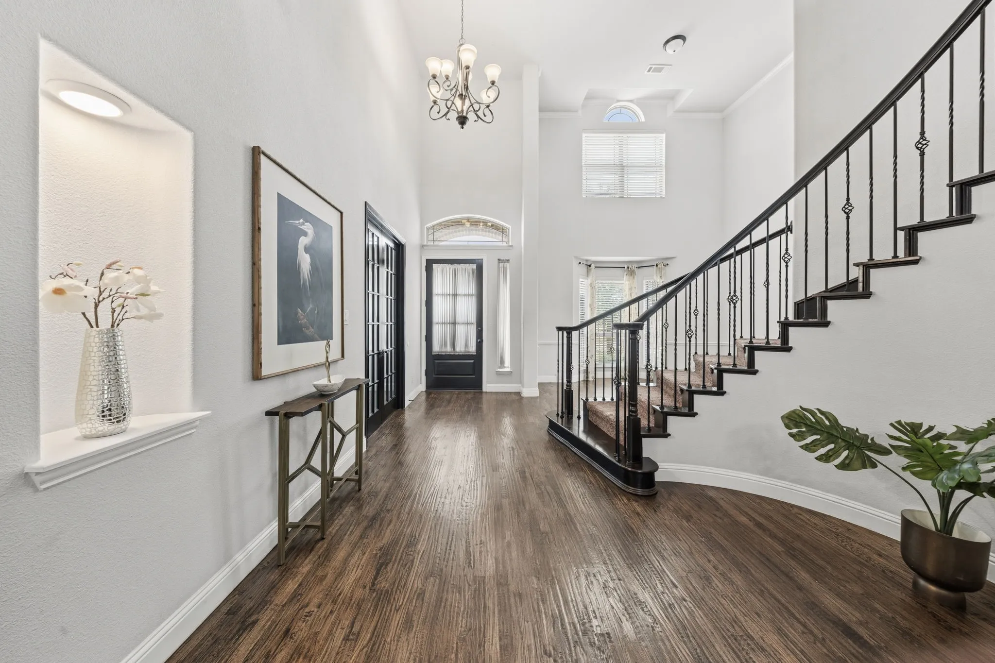 Two-story foyer with dark wood-finish flooring, a grand staircase with wrought iron balusters, a decorative chandelier, and an arched transom window above the entry door