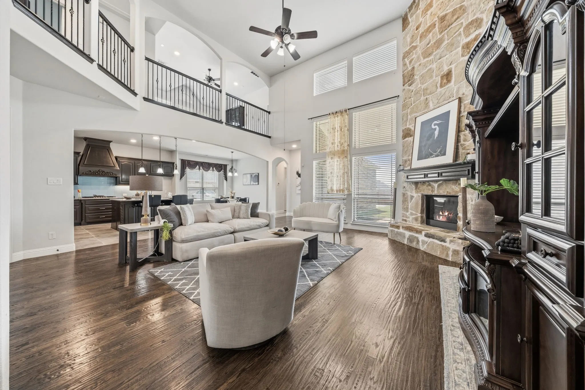 Living area with wood-finish flooring, a two-story stone-faced fireplace, and high ceilings