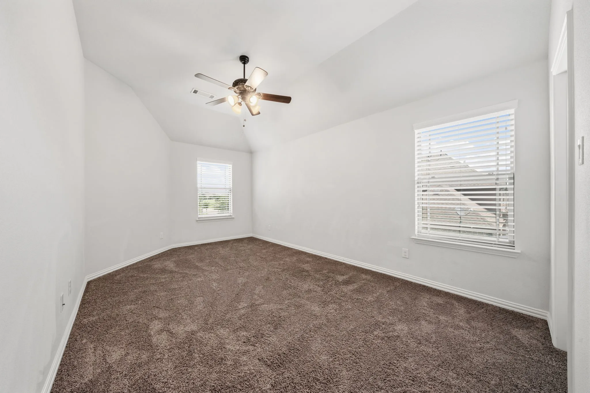 Carpeted room featuring two windows with horizontal blinds, a vaulted ceiling, and a ceiling fan with integrated lighting