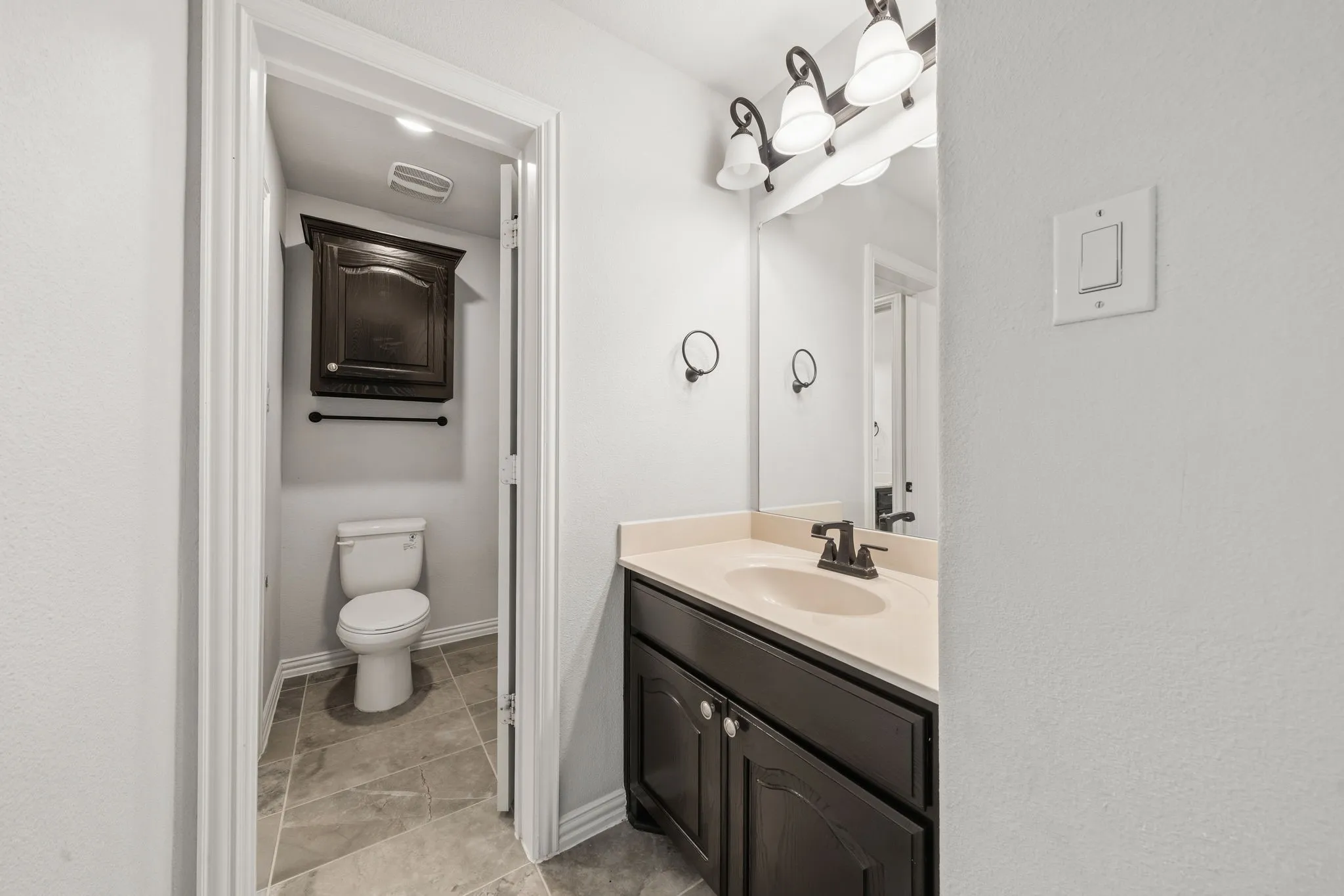 Bathroom vanity featuring a light-colored countertop, dark wood-finish cabinetry, and a bronze-finish faucet