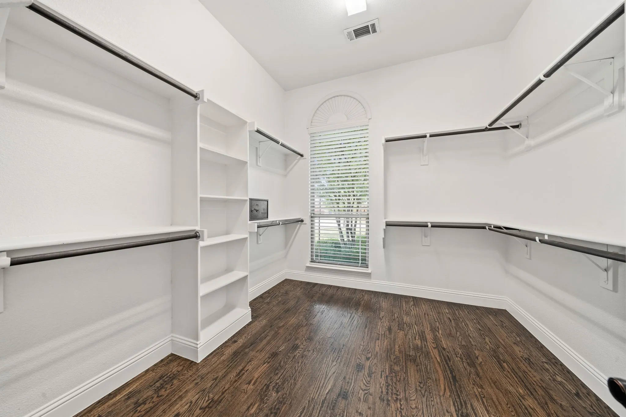Spacious walk-in closet featuring wood-finish flooring, extensive built-in shelving, and multiple hanging rods