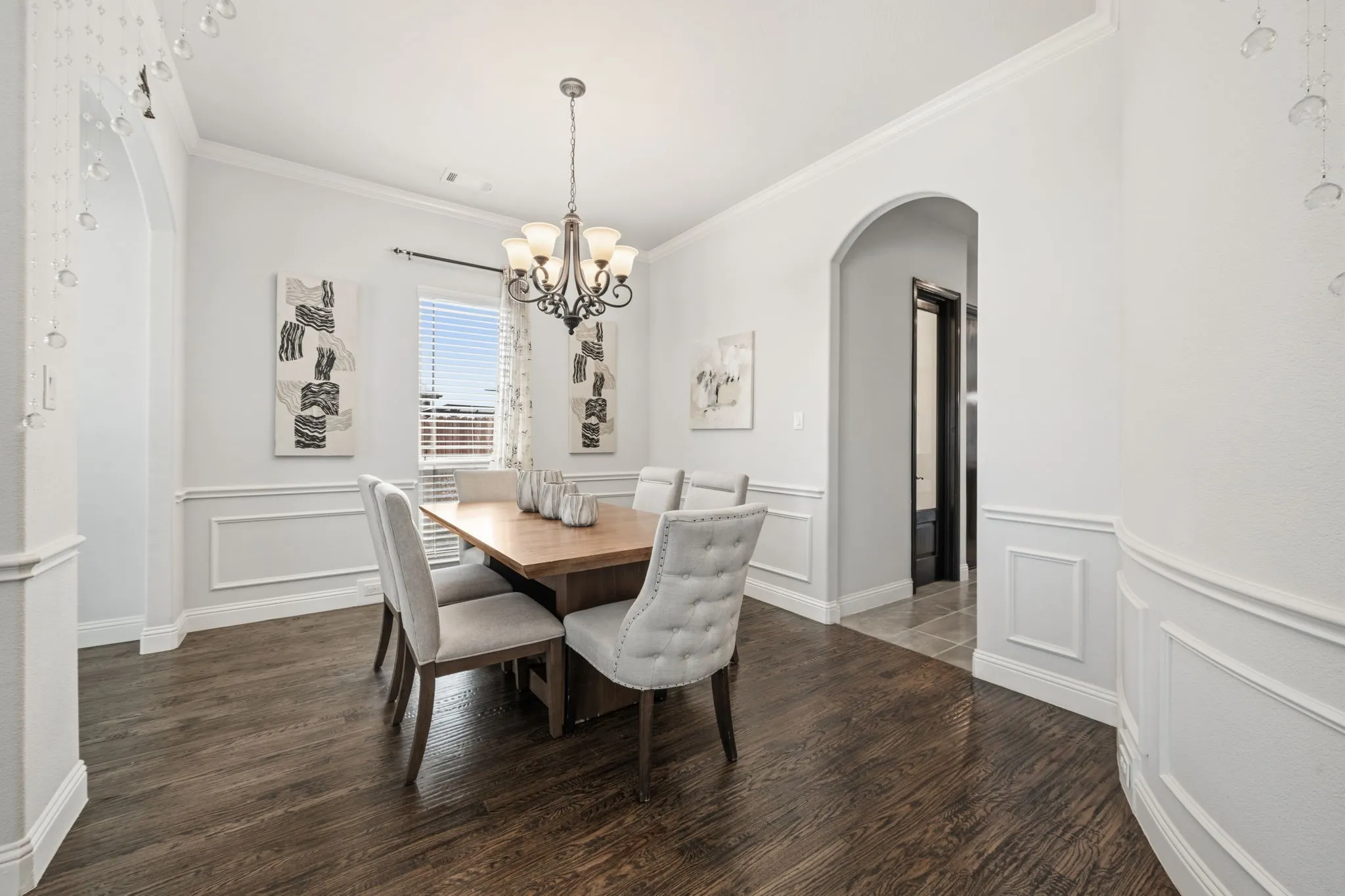 Formal dining space featuring wood-finish flooring, wainscoting, and an arched entry