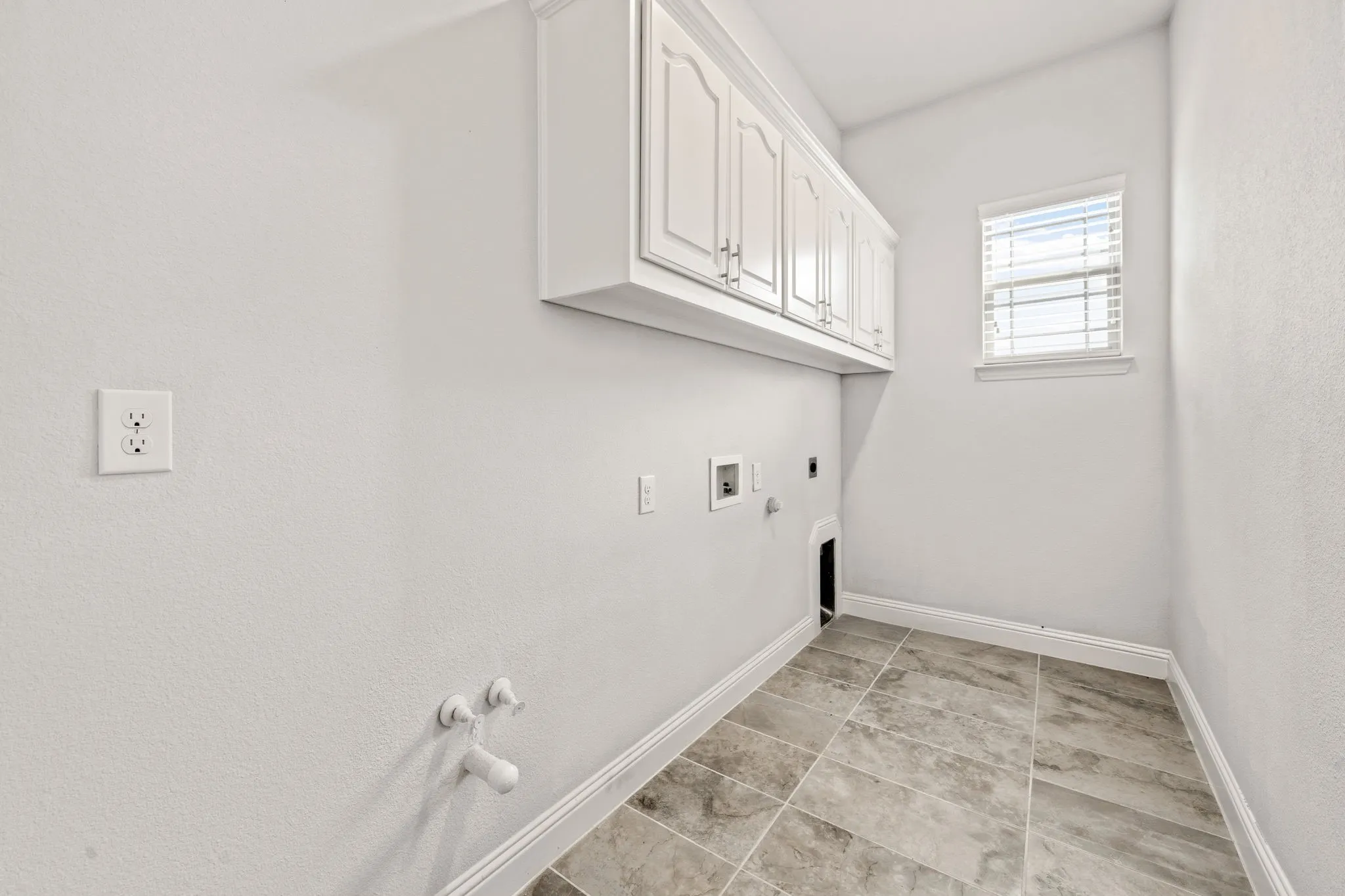 Dedicated utility room featuring upper cabinetry, tile flooring, window with blinds, and appliance hookups
