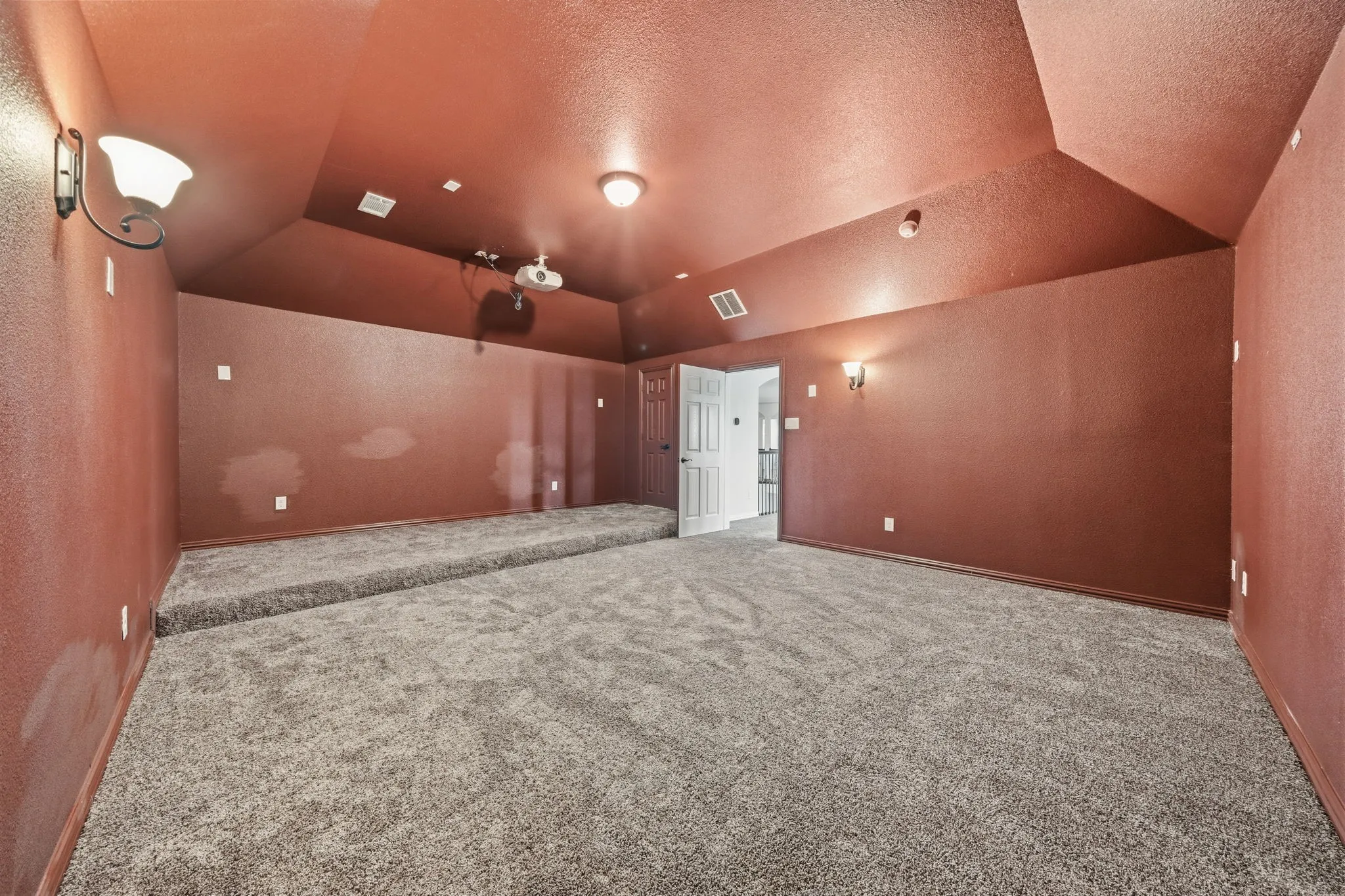 Spacious room featuring textured walls, sloped ceilings, wall-mounted sconces, recessed lighting, and a raised platform