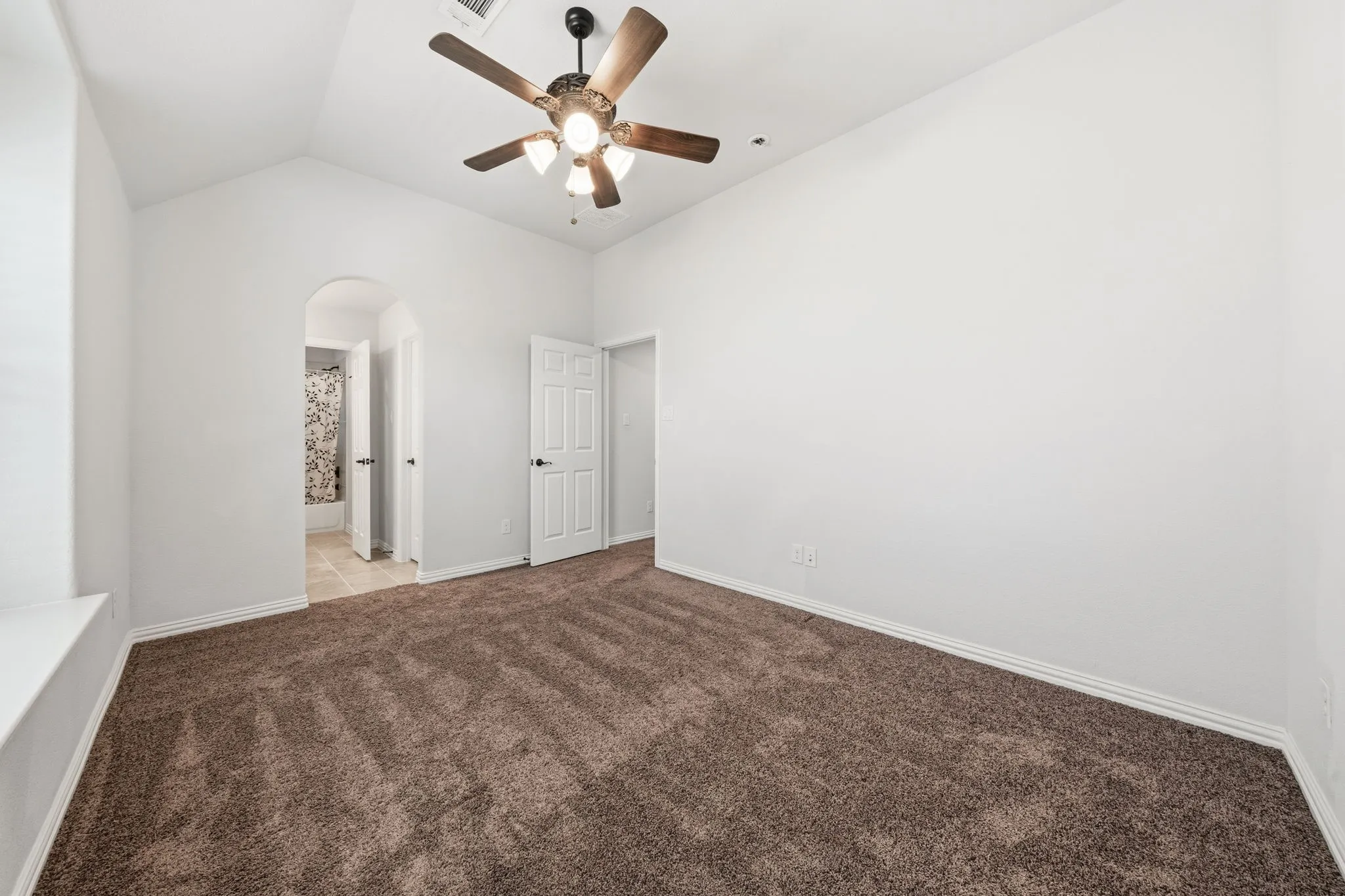 Spacious room featuring vaulted ceilings, a ceiling fan with integrated lighting, and plush brown carpeting