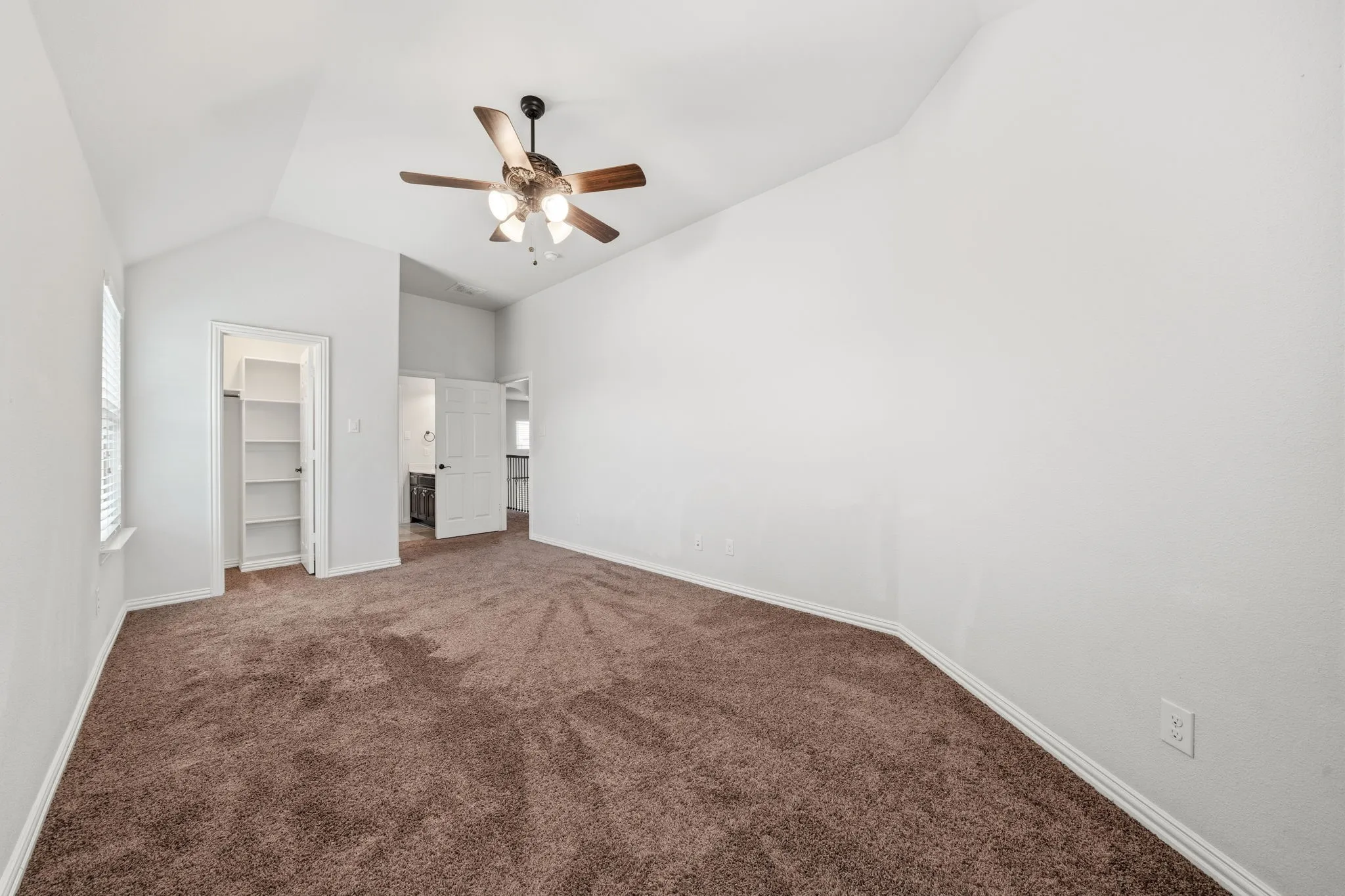 Spacious room featuring vaulted ceilings, brown carpet flooring, and a ceiling fan with integrated lighting