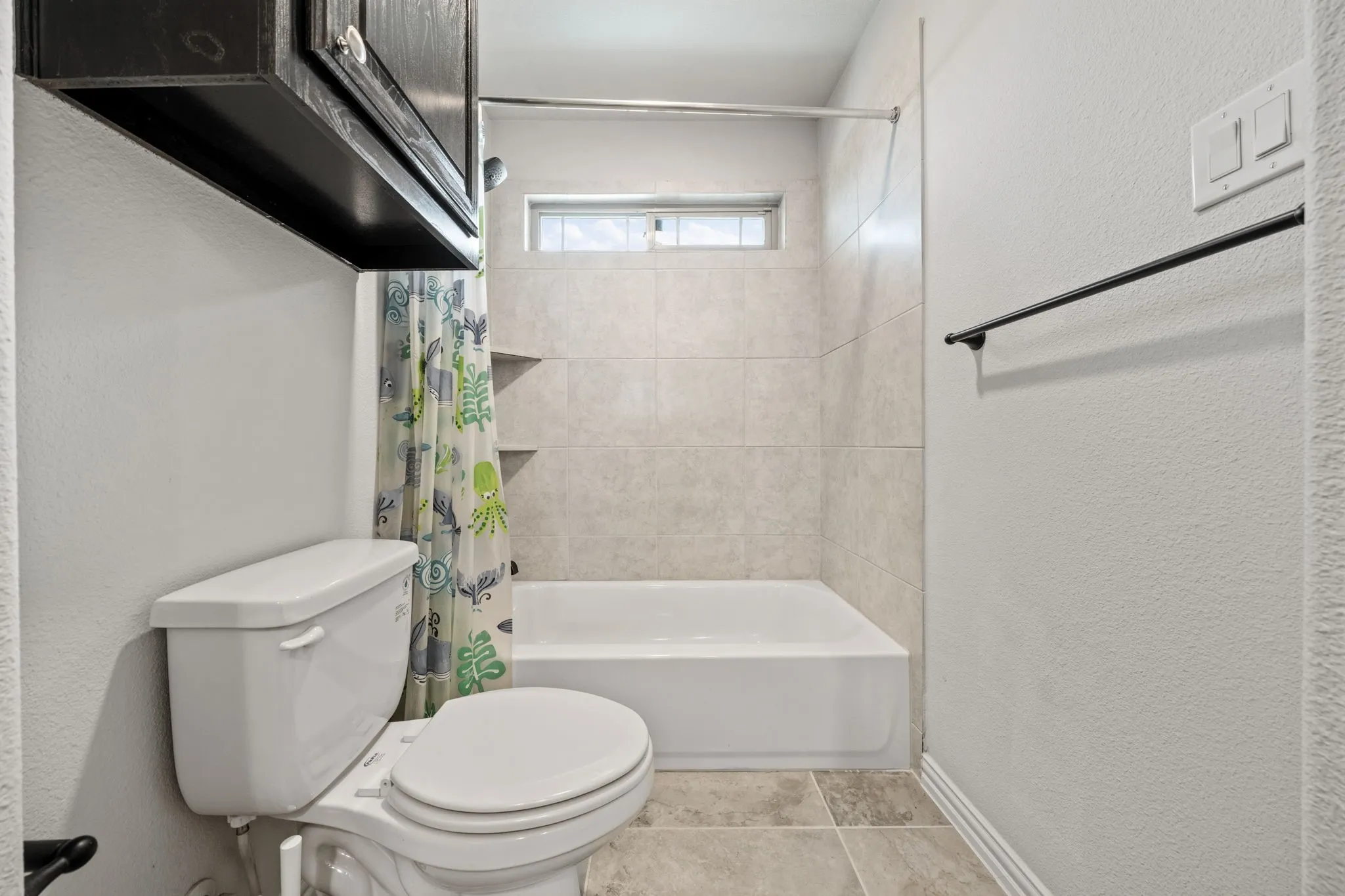 Bathroom featuring a white tub, light-toned tile surround, and a high horizontal window