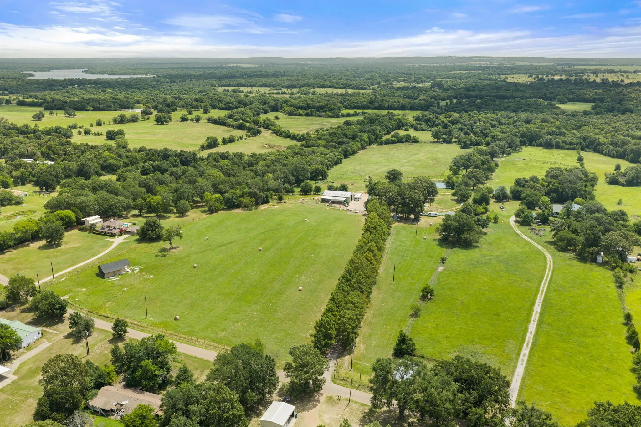 Expansive rural landscape featuring lush green fields, scattered mature trees, and a distant body of water