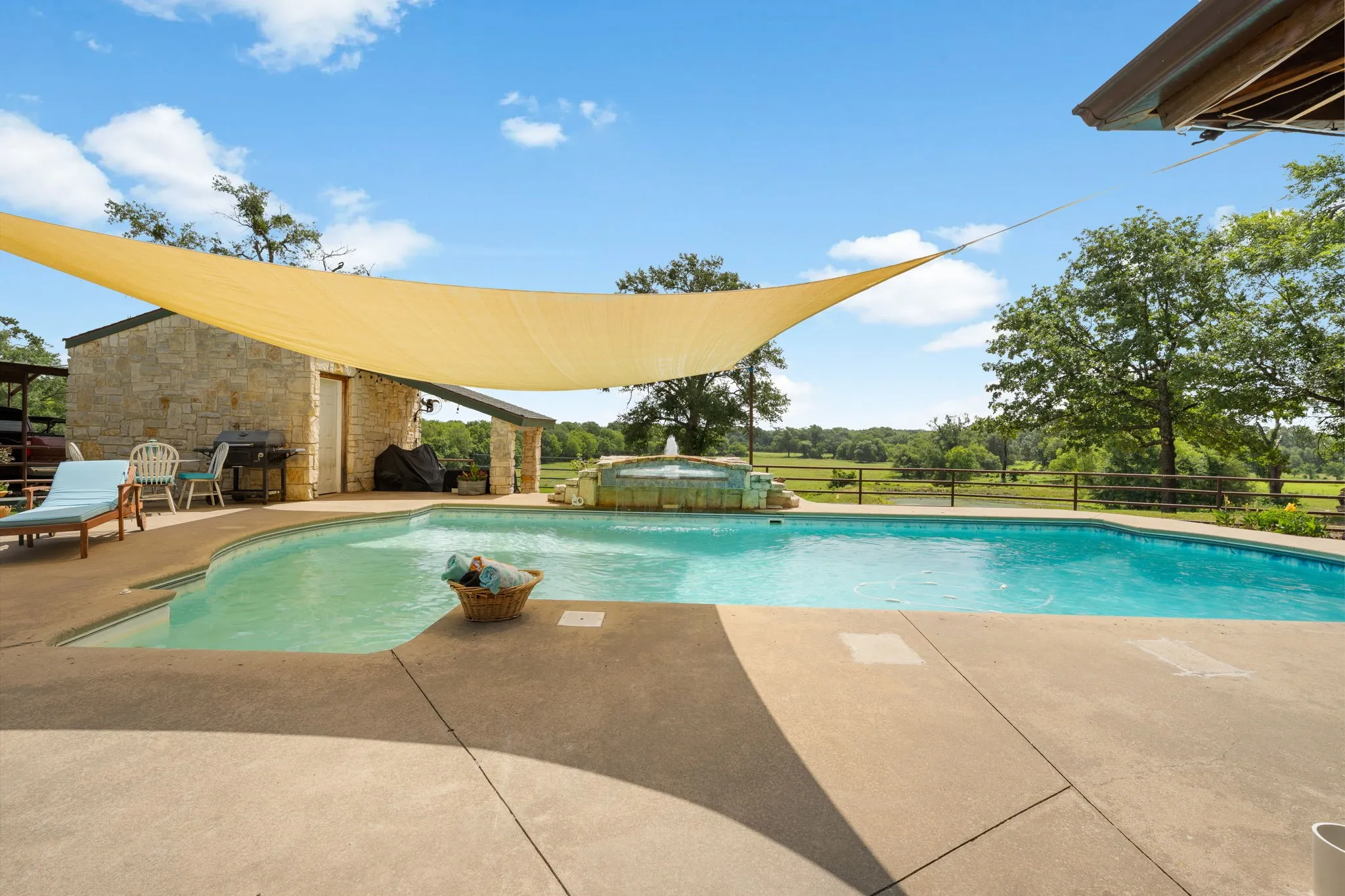 In-ground swimming pool with a concrete deck, an integrated water feature, and a stone-clad pool house