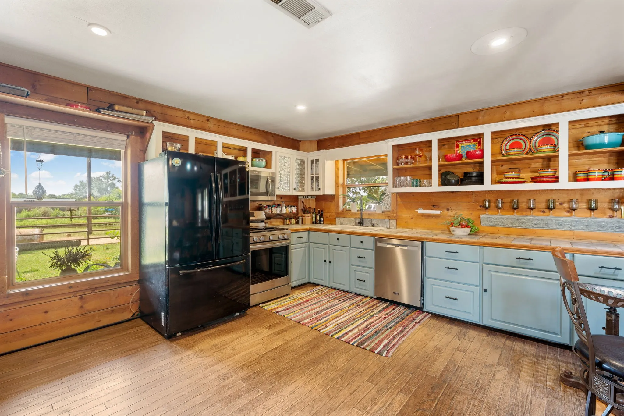 Kitchen featuring wood-finish flooring, wood plank walls, light blue lower cabinetry, stainless steel appliances, and open shelving