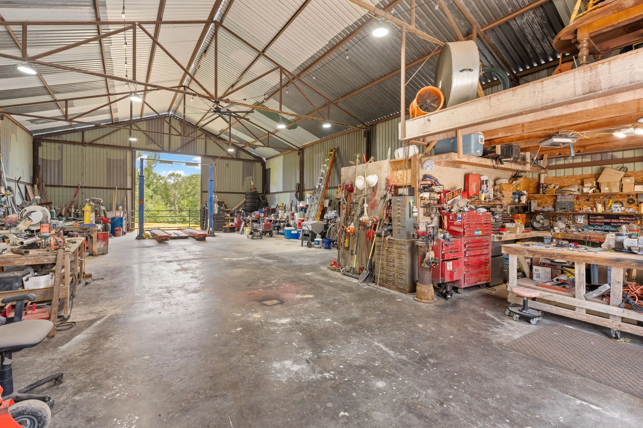 Spacious metal-sided workshop featuring a concrete floor, high-bay lighting, open rafter ceiling, and a vehicle lift