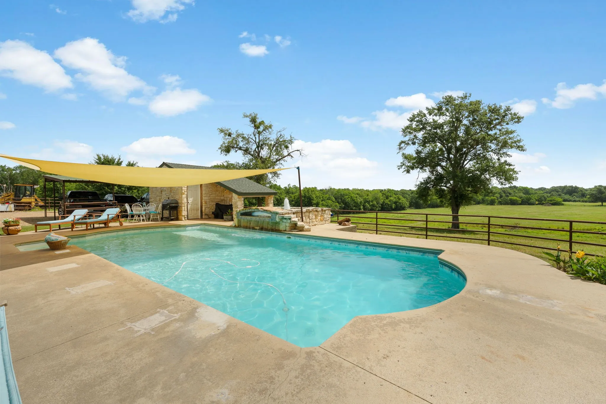 Outdoor pool with expansive concrete decking, stone-clad outdoor kitchen structure, and a secondary spa feature