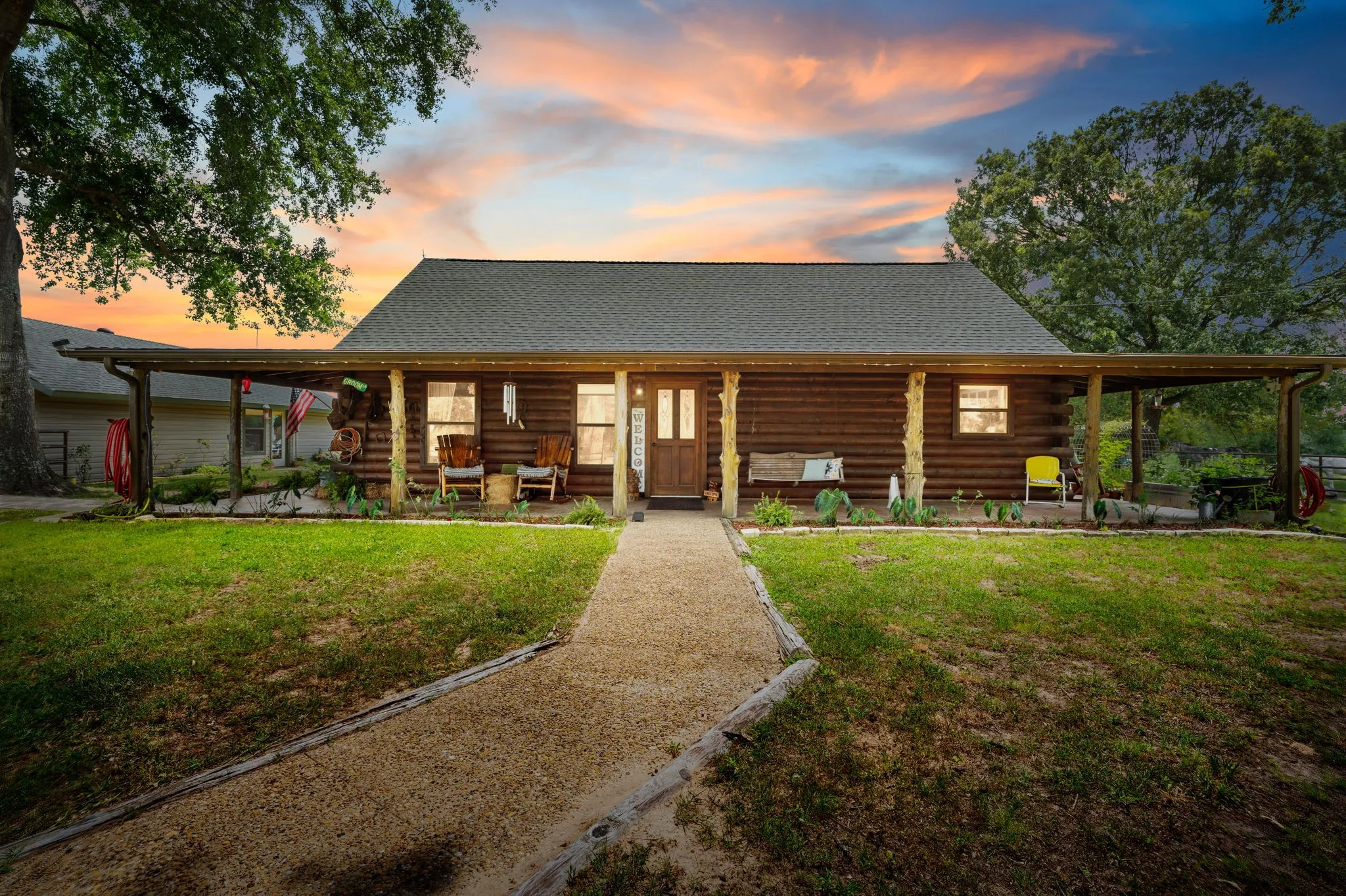 Log cabin exterior featuring a covered front porch, gravel pathway, and mature trees