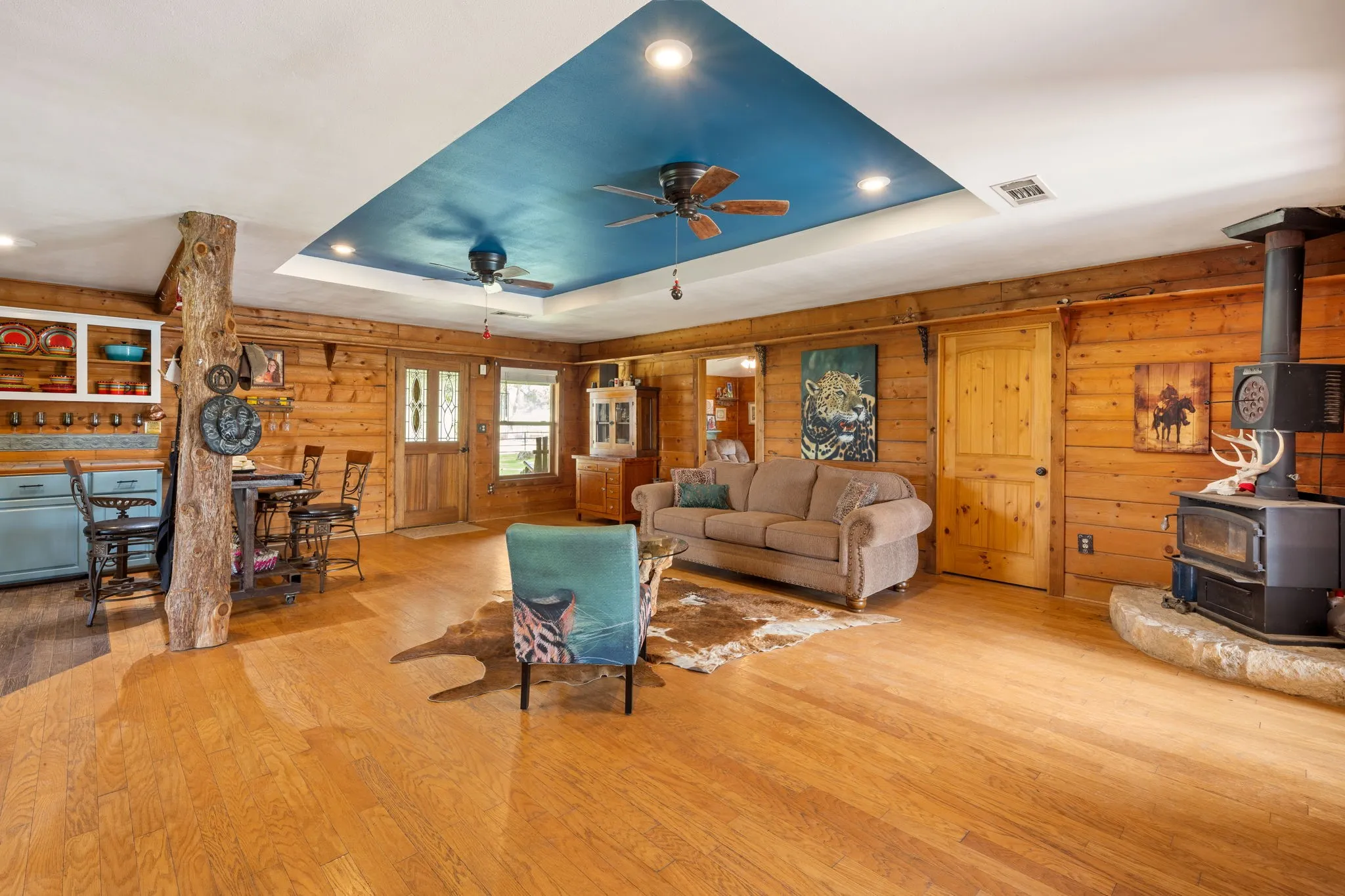 Spacious living area featuring wood-finish flooring, wood-paneled walls, and a recessed ceiling with a blue accent panel
