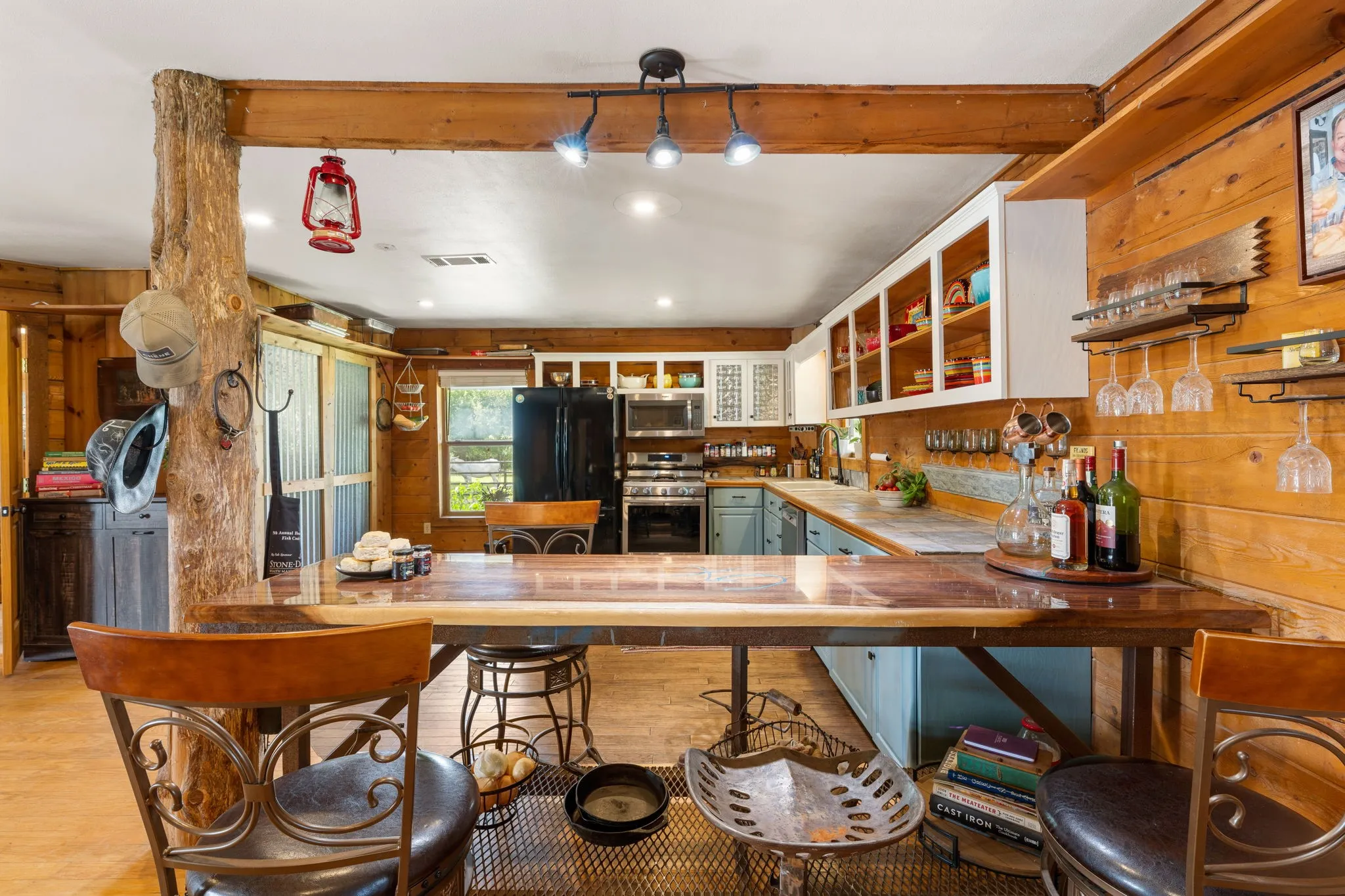 Kitchen featuring wood-paneled walls, a natural wood beam, track lighting, light blue lower cabinetry, white open upper shelving, and a dark wood-finish countertop