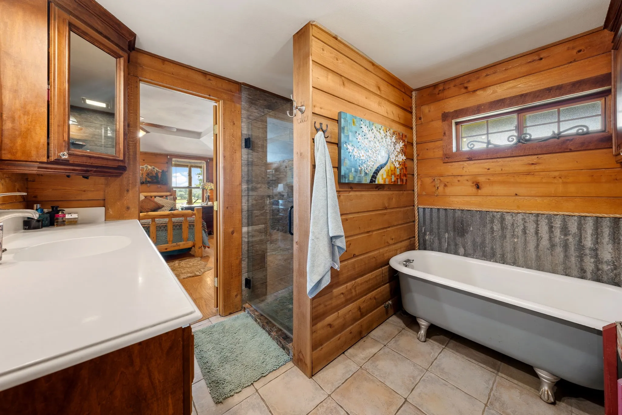 Bathroom featuring a white vanity with integrated sink, wood-finish cabinetry, a glass-enclosed shower, a clawfoot bathtub, and tile flooring