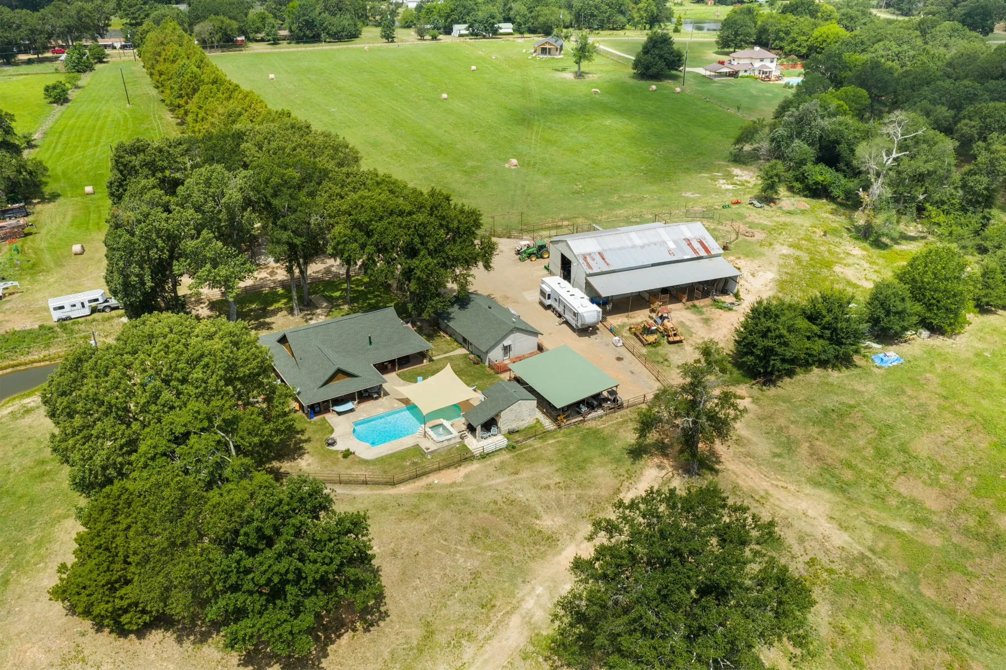 Expansive property featuring a main residence with a swimming pool, detached covered patio, a large barn, and surrounding green acreage