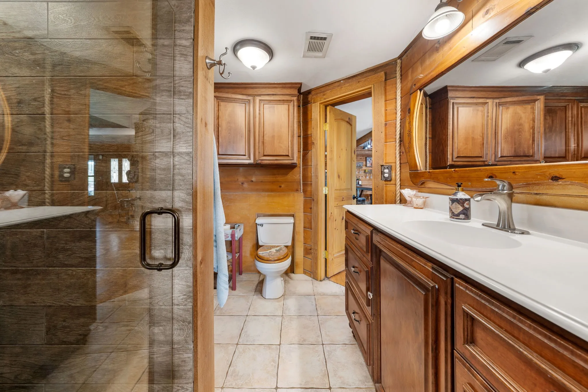 Bathroom featuring a clear glass shower enclosure, wood-paneled walls, a single vanity with a white countertop and dark wood cabinetry, and tiled flooring