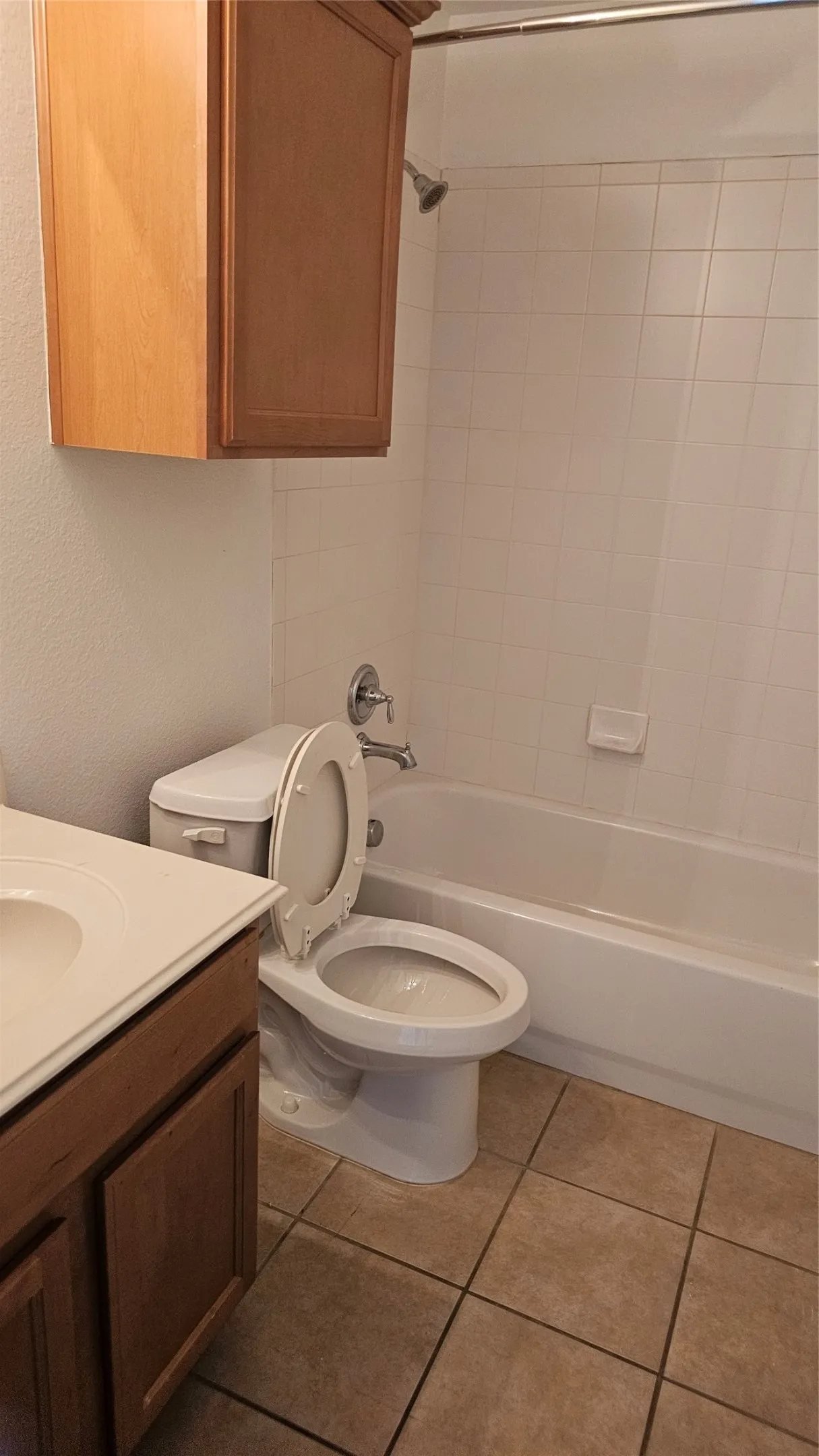 Bathroom with a built-in wood cabinet, a white toilet, a shower/tub combination with white subway tile surround, and neutral-toned tile flooring