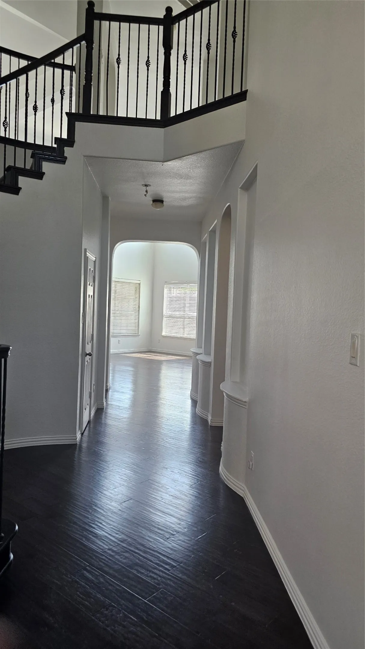 Grand entryway featuring dark wood-finish flooring, a prominent staircase with wrought iron balusters, arched hallway openings, and built-in wall niches