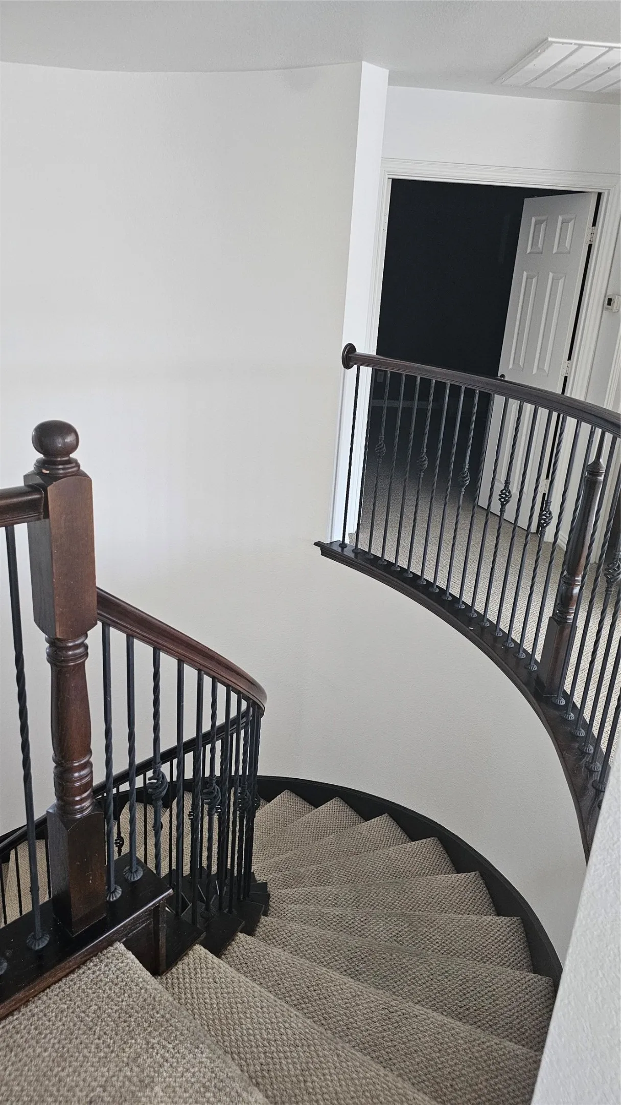 Curved staircase featuring dark wood newel posts and handrails with black wrought iron balusters