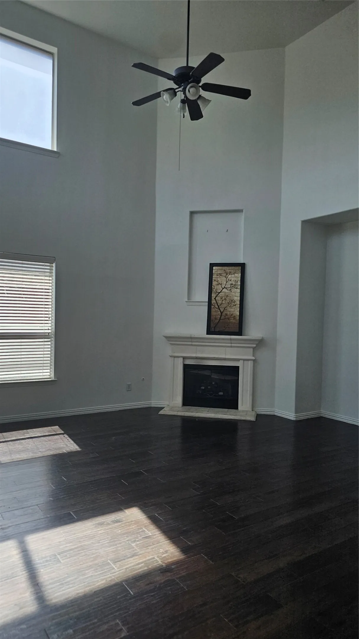 Vaulted ceilings with a ceiling fan, a fireplace with a mantel, dark wood-finish flooring, and multiple windows with blinds