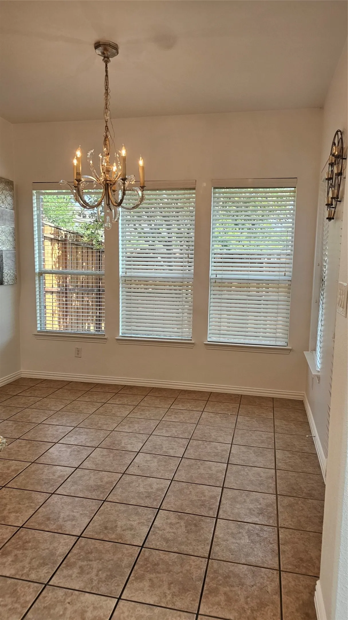Room featuring light-toned square tile flooring, multiple windows with blinds, a crystal chandelier, and white wall finishes