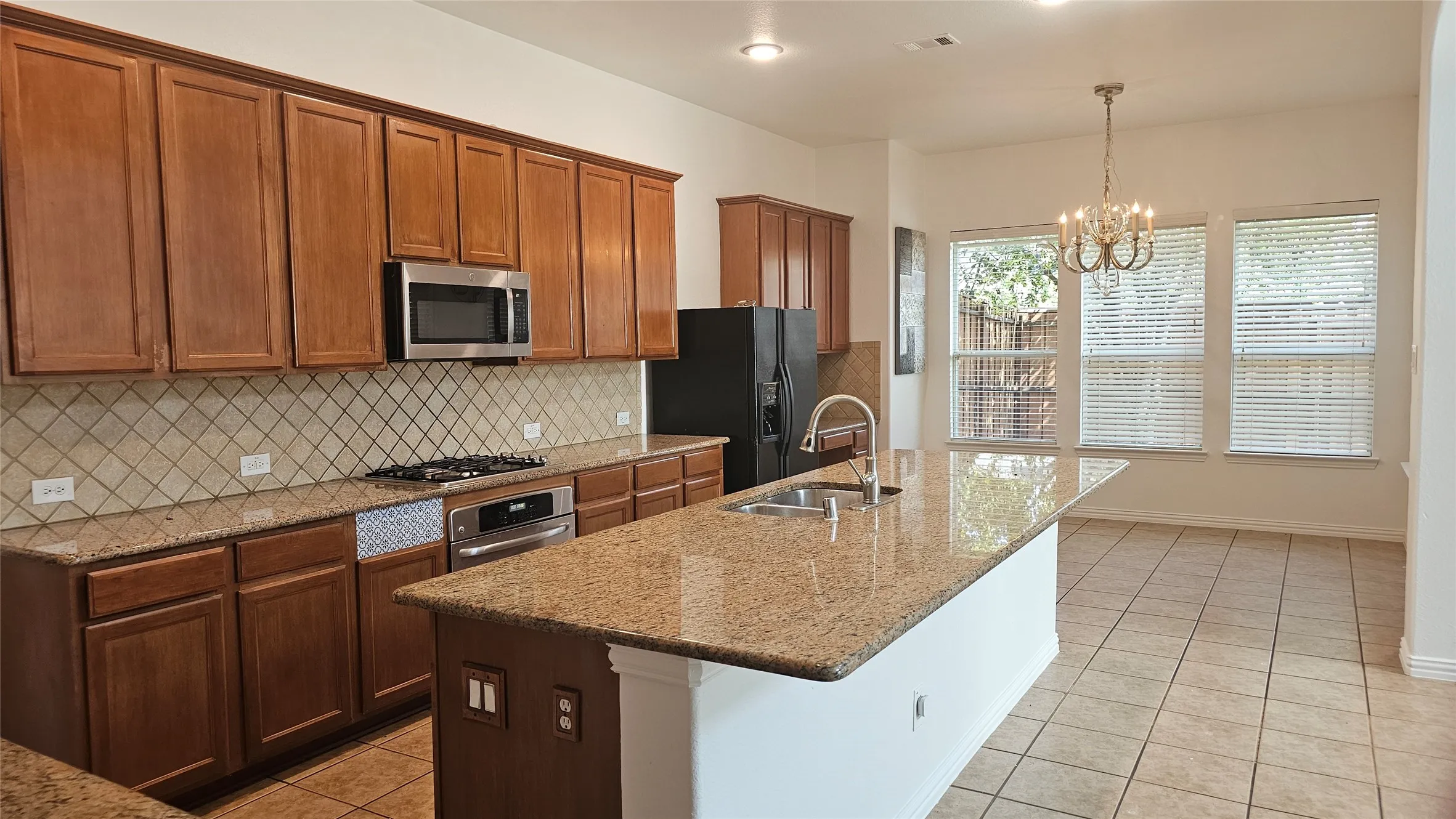 Kitchen featuring wood cabinetry, stainless steel appliances, granite countertops, and a central island with an undermount sink