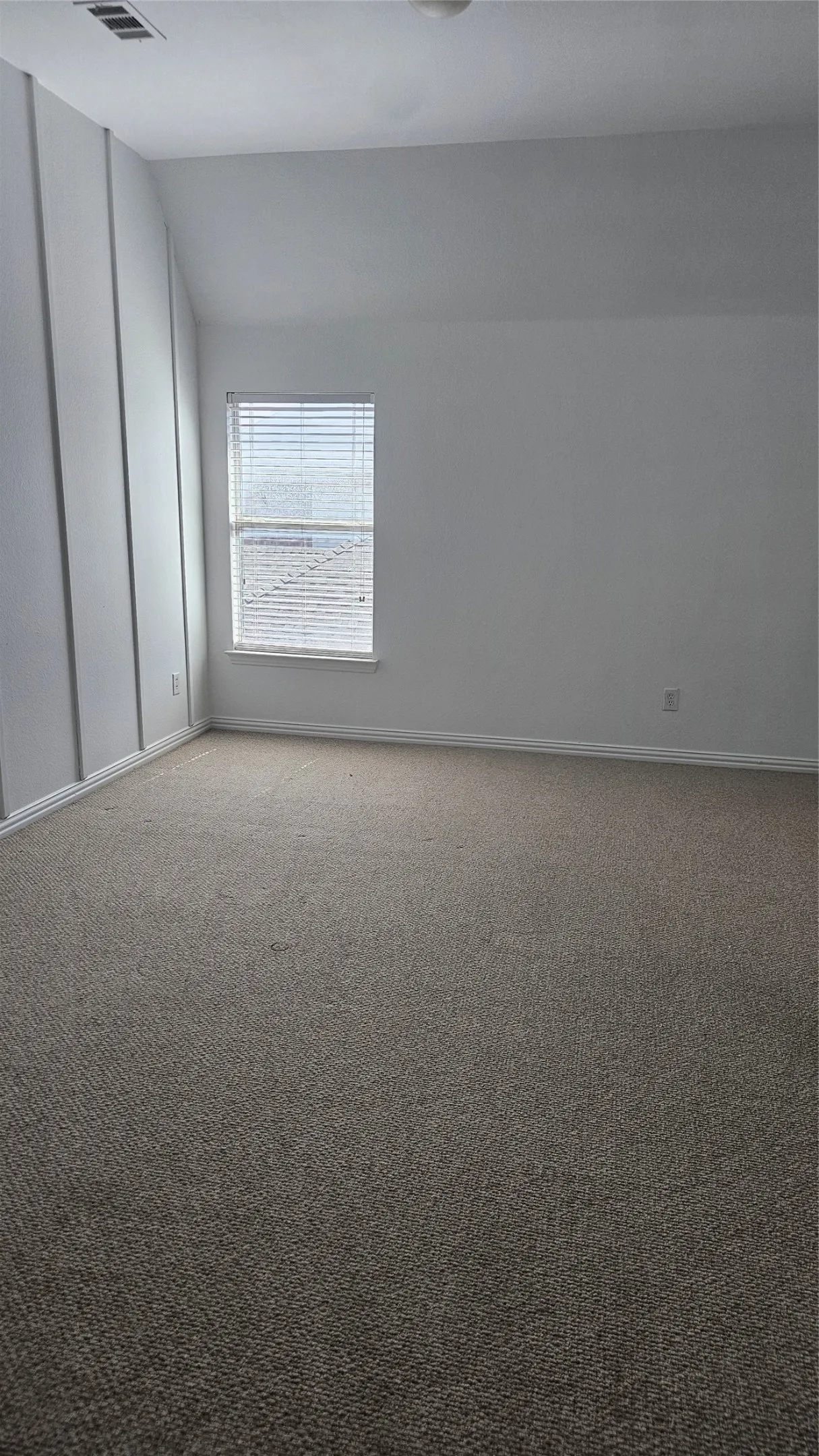 Spacious room featuring neutral carpeting, white wall paint, and a window with horizontal blinds
