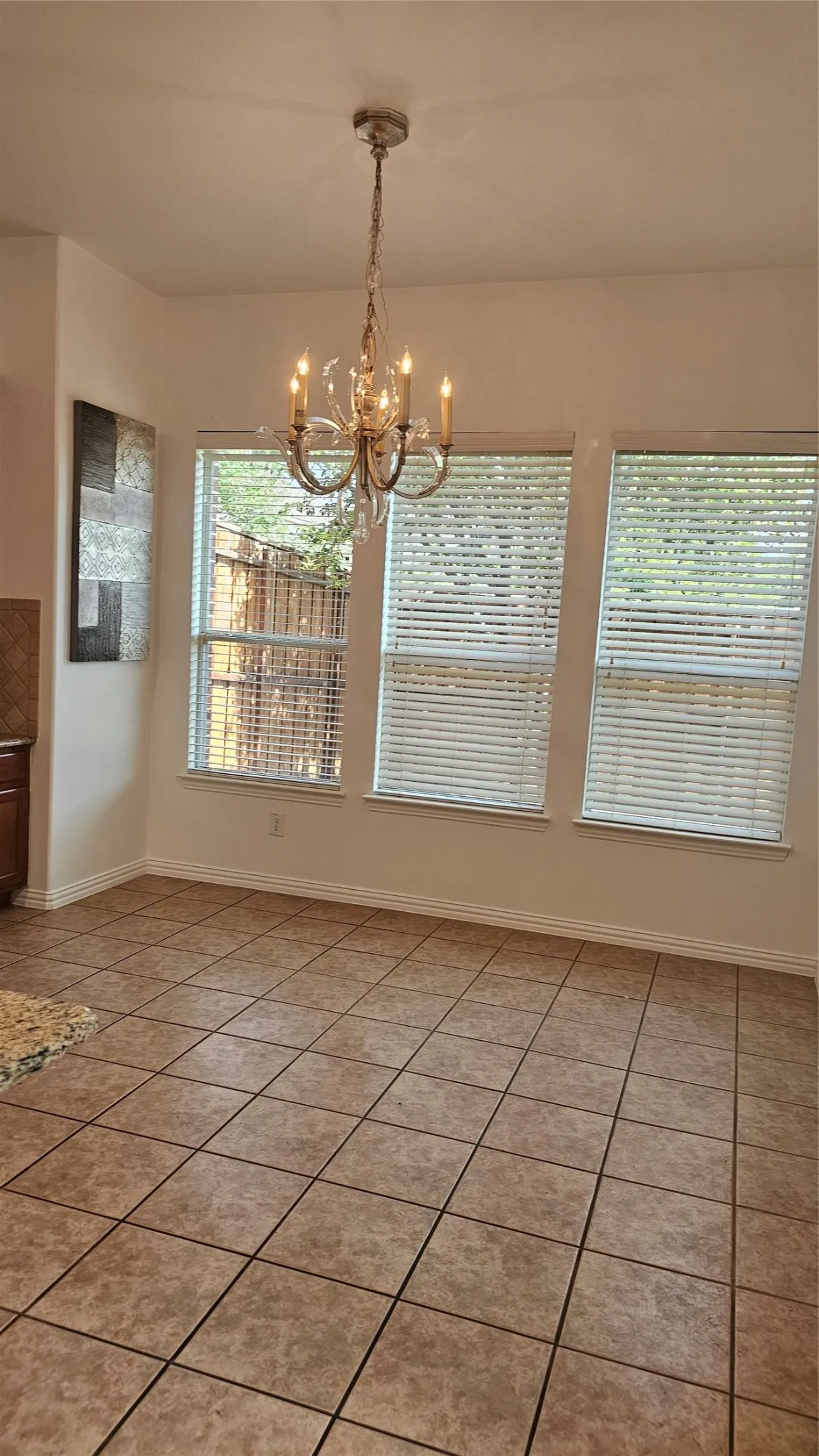 Dining area featuring a decorative chandelier, three large windows with blinds, and durable tile flooring